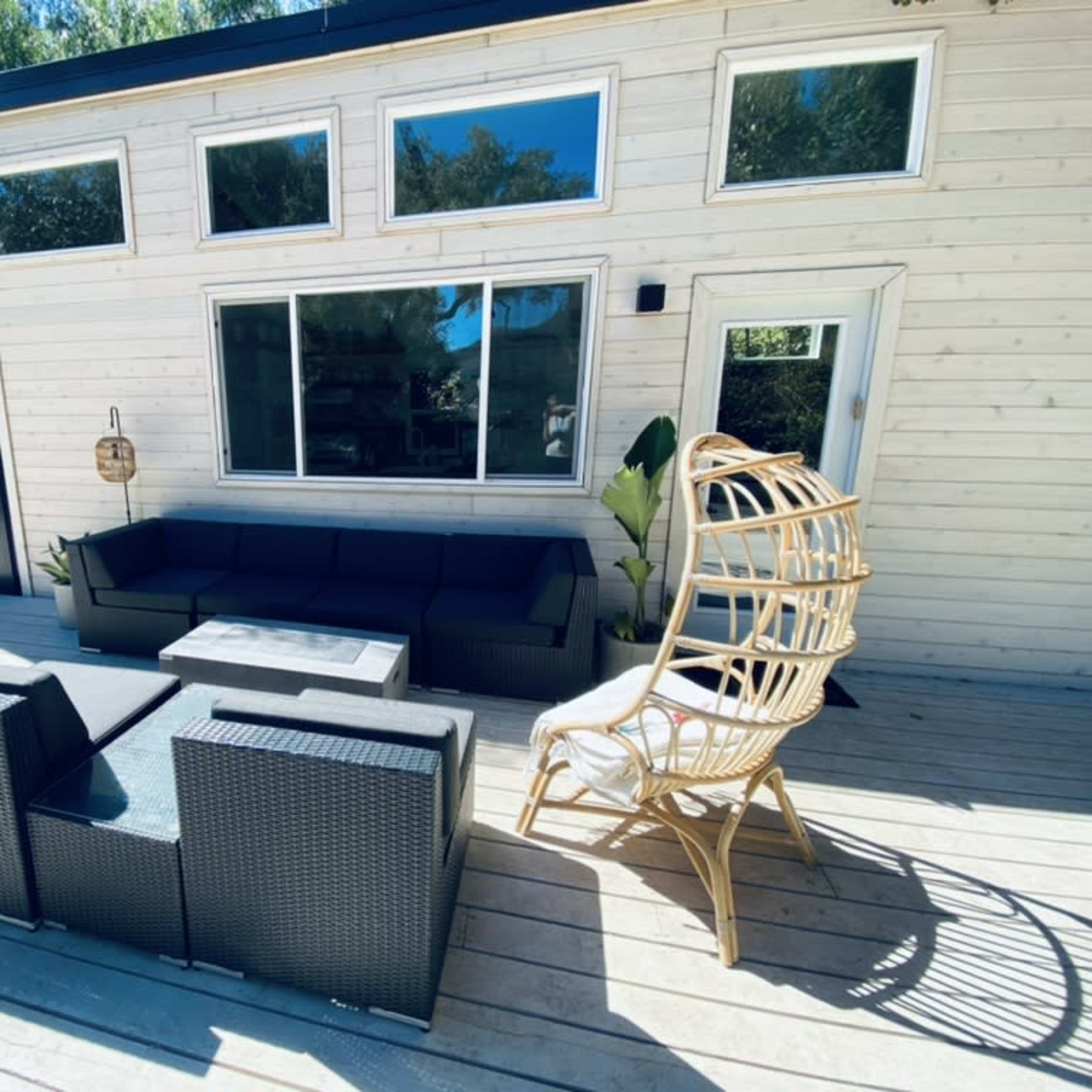 A modern wooden house with large windows, a black accent wall, a patio area with a sectional sofa, a coffee table, and a wicker chair.