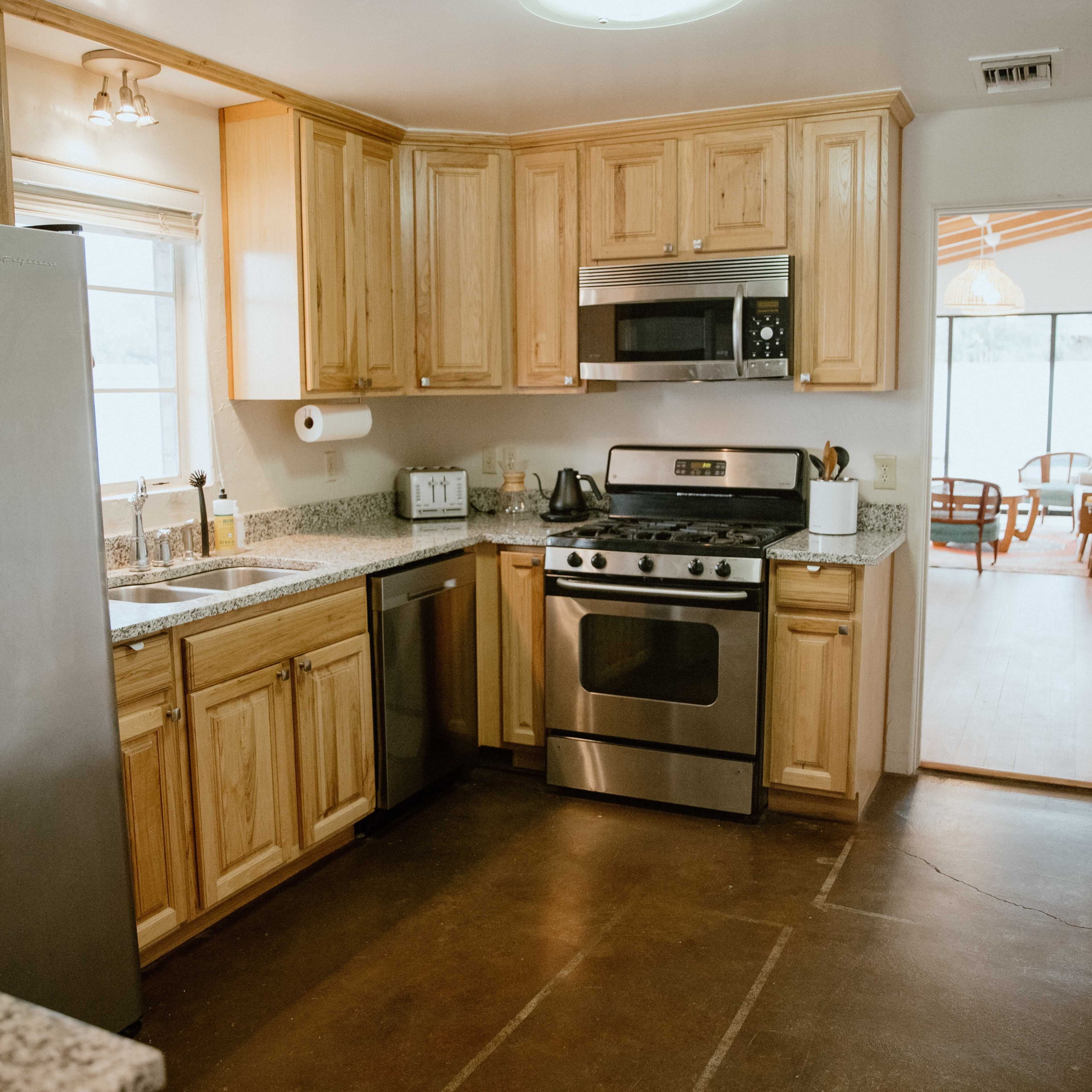 A modern kitchen features wooden cabinetry, stainless steel appliances, and a granite countertop with a view of an adjoining room.