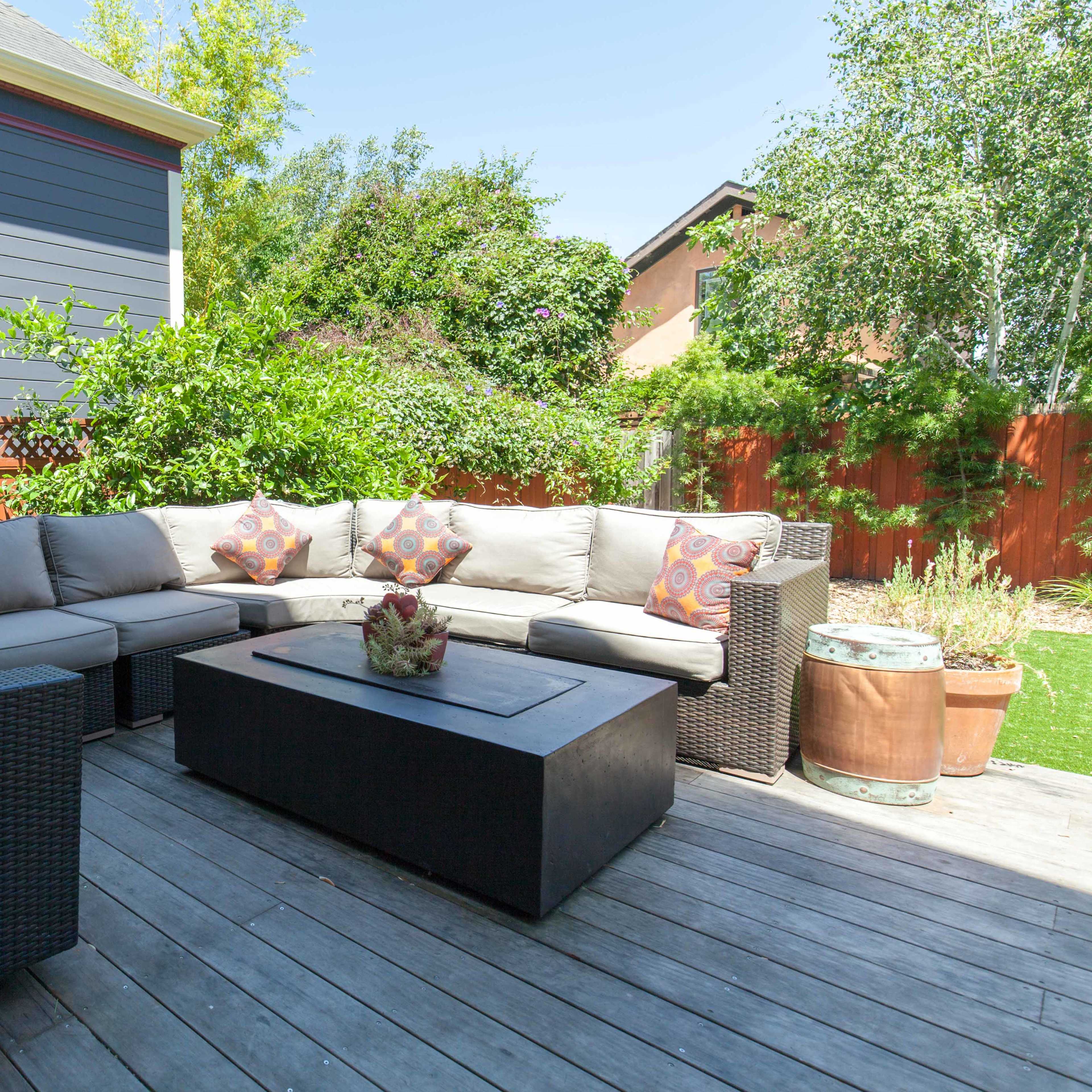 A spacious outdoor seating area features a sectional sofa and a coffee table on a wooden deck surrounded by greenery.