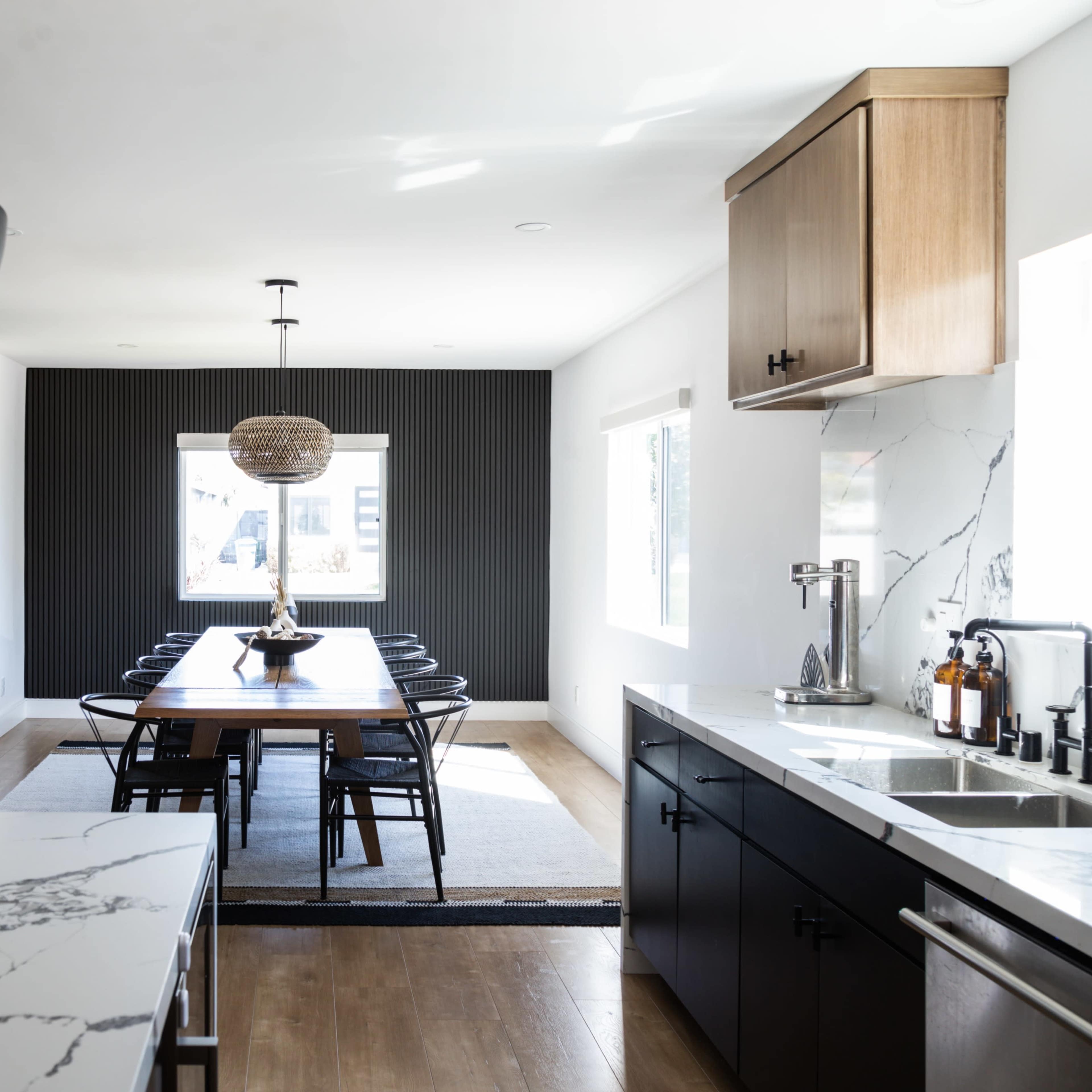 A modern kitchen area features a marble countertop island and a dining table surrounded by black chairs, with a large window illuminating the space.
