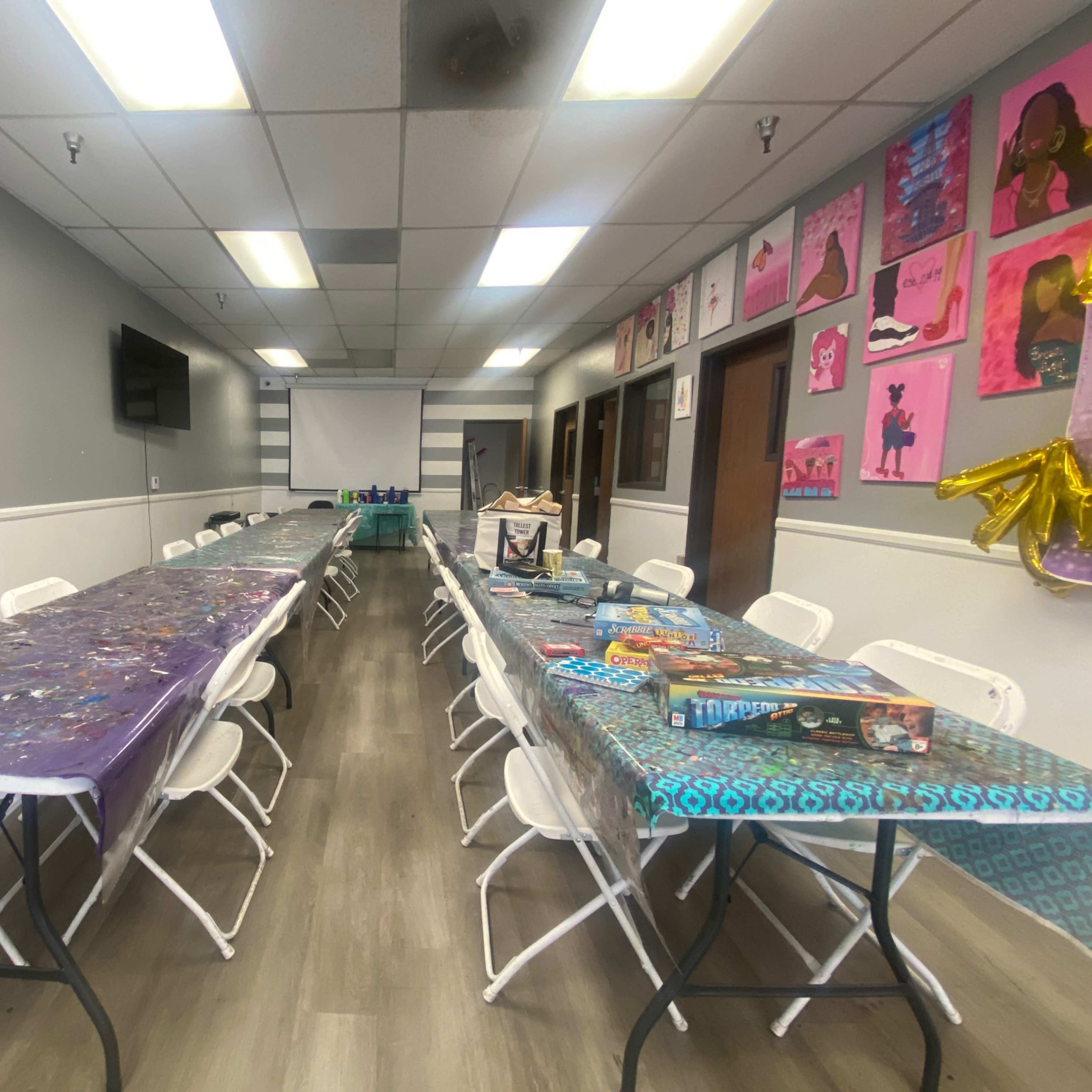 A long, narrow room with two rows of tables covered in colorful tablecloths and white chairs arranged along each side.