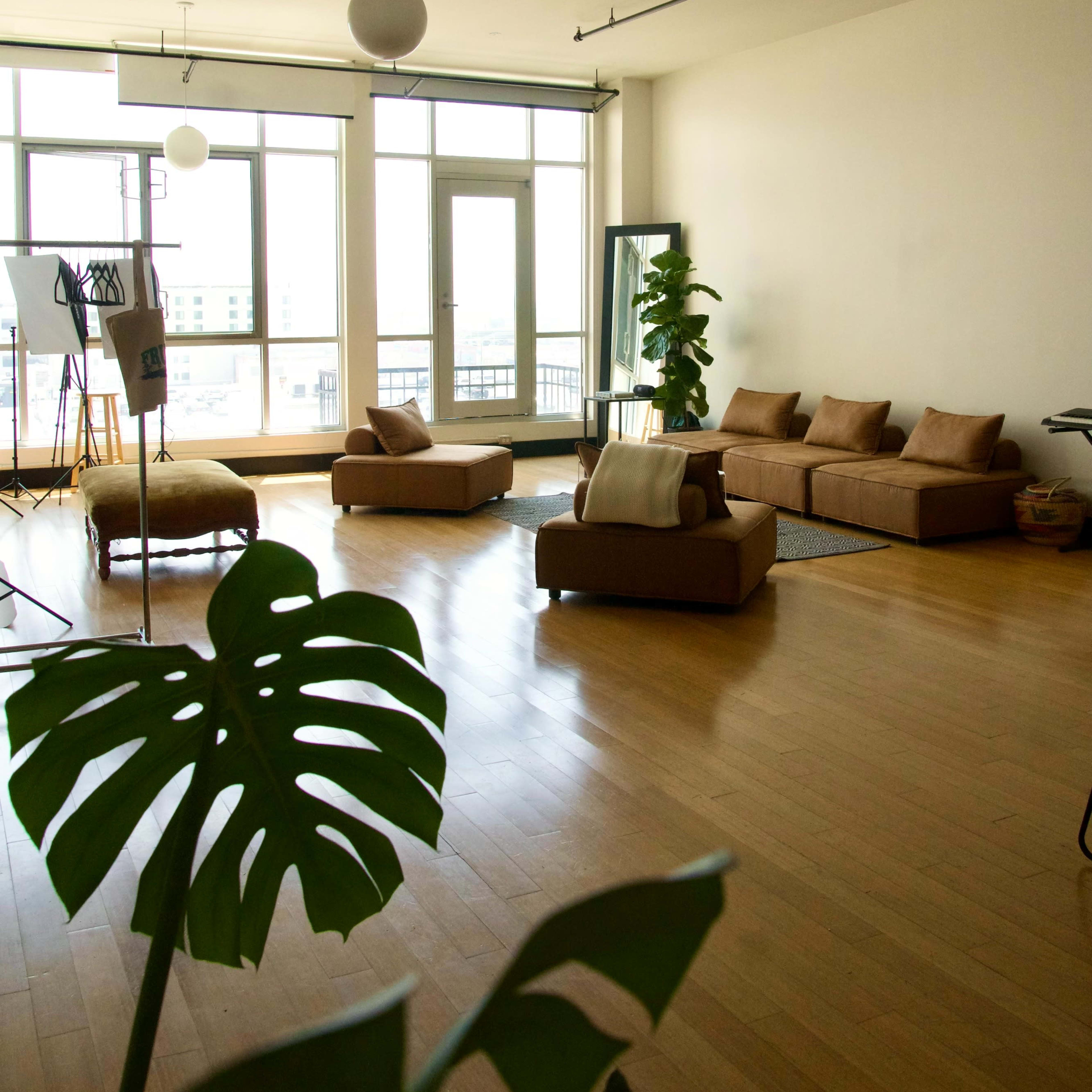 A spacious, minimalist living room with a large window, several couches, and a plant in the foreground.
