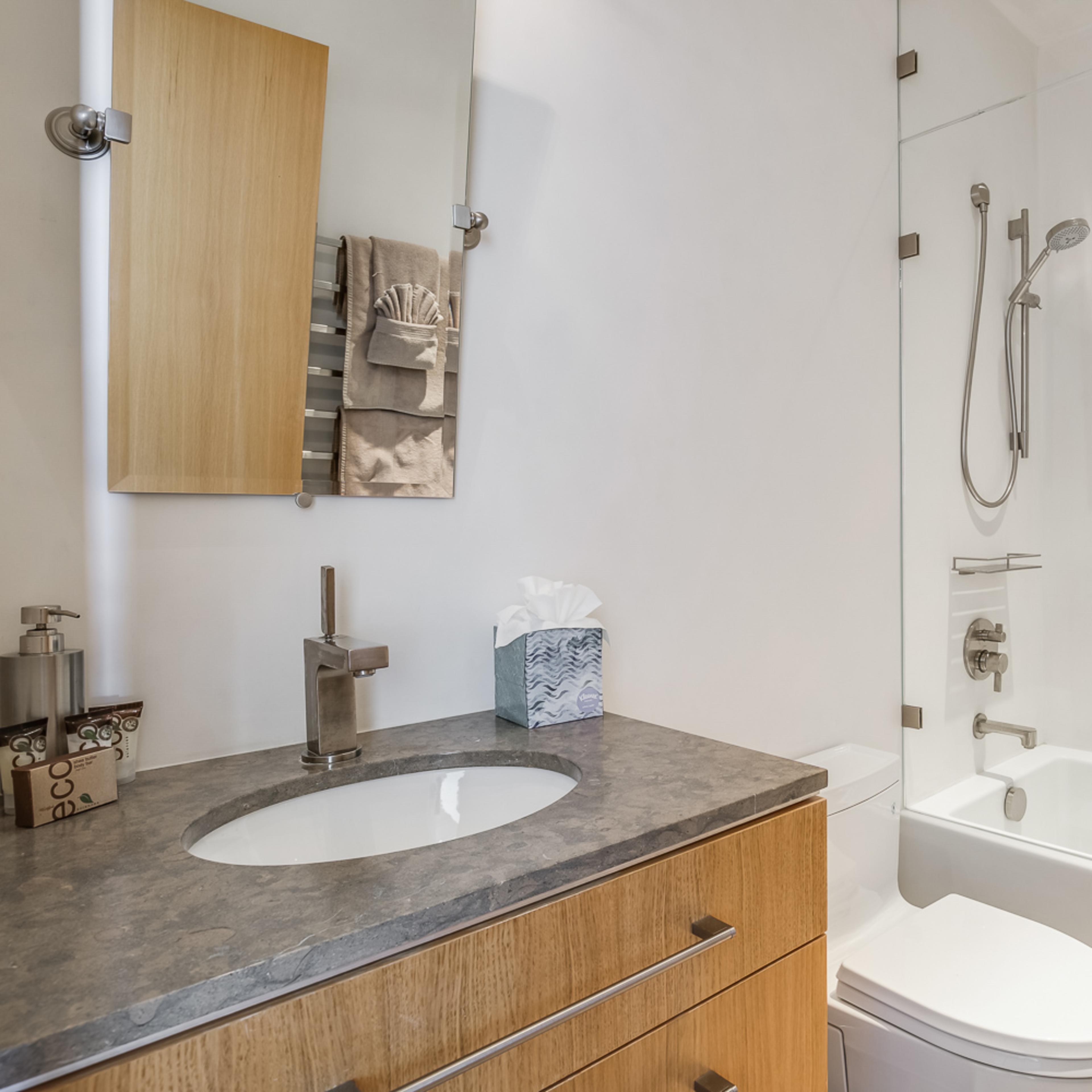 A modern bathroom featuring a glass shower, a bathtub, a vanity with a circular sink, and a large mirror.