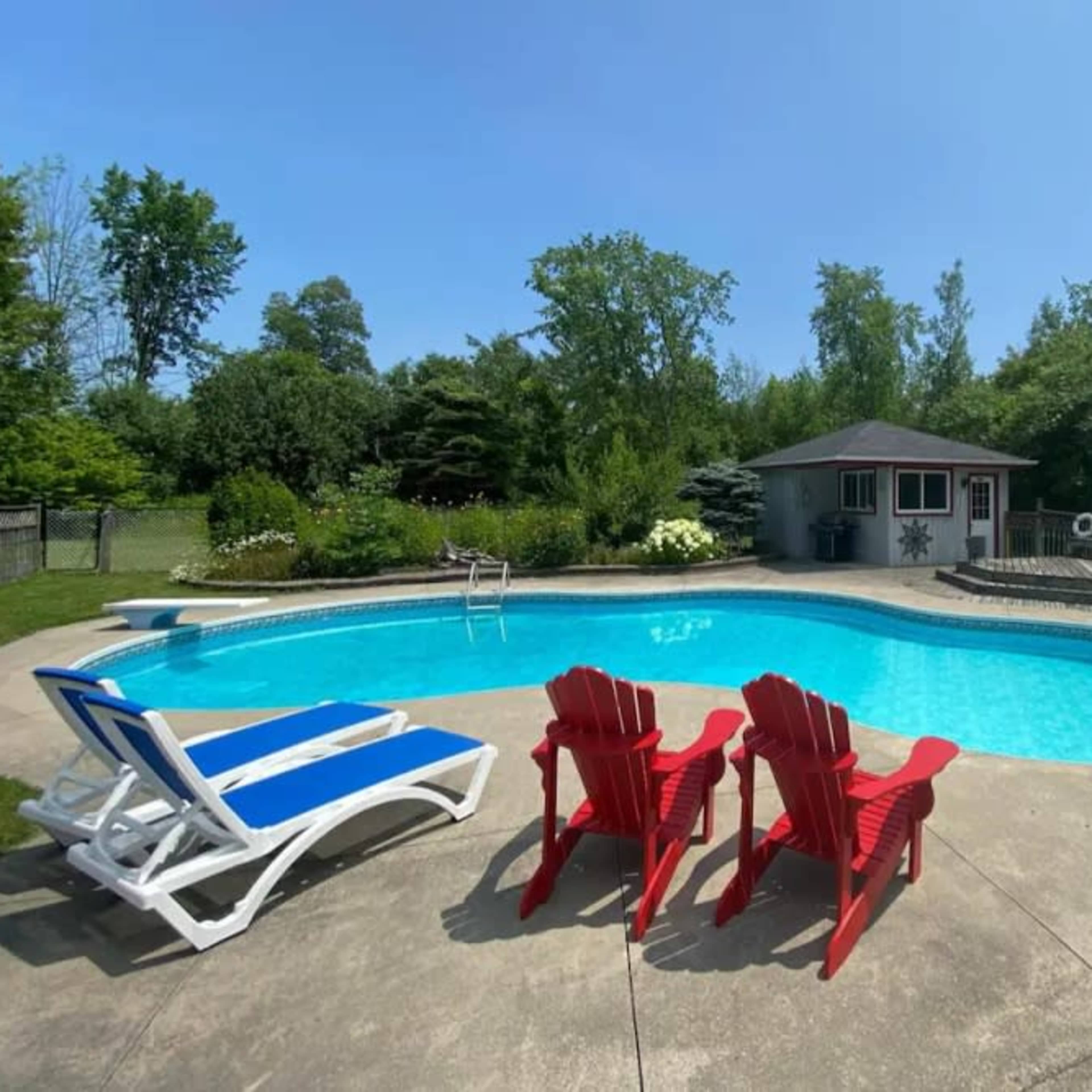 A spacious in-ground pool surrounded by red lounge chairs and a shaded cabana in a landscaped backyard.