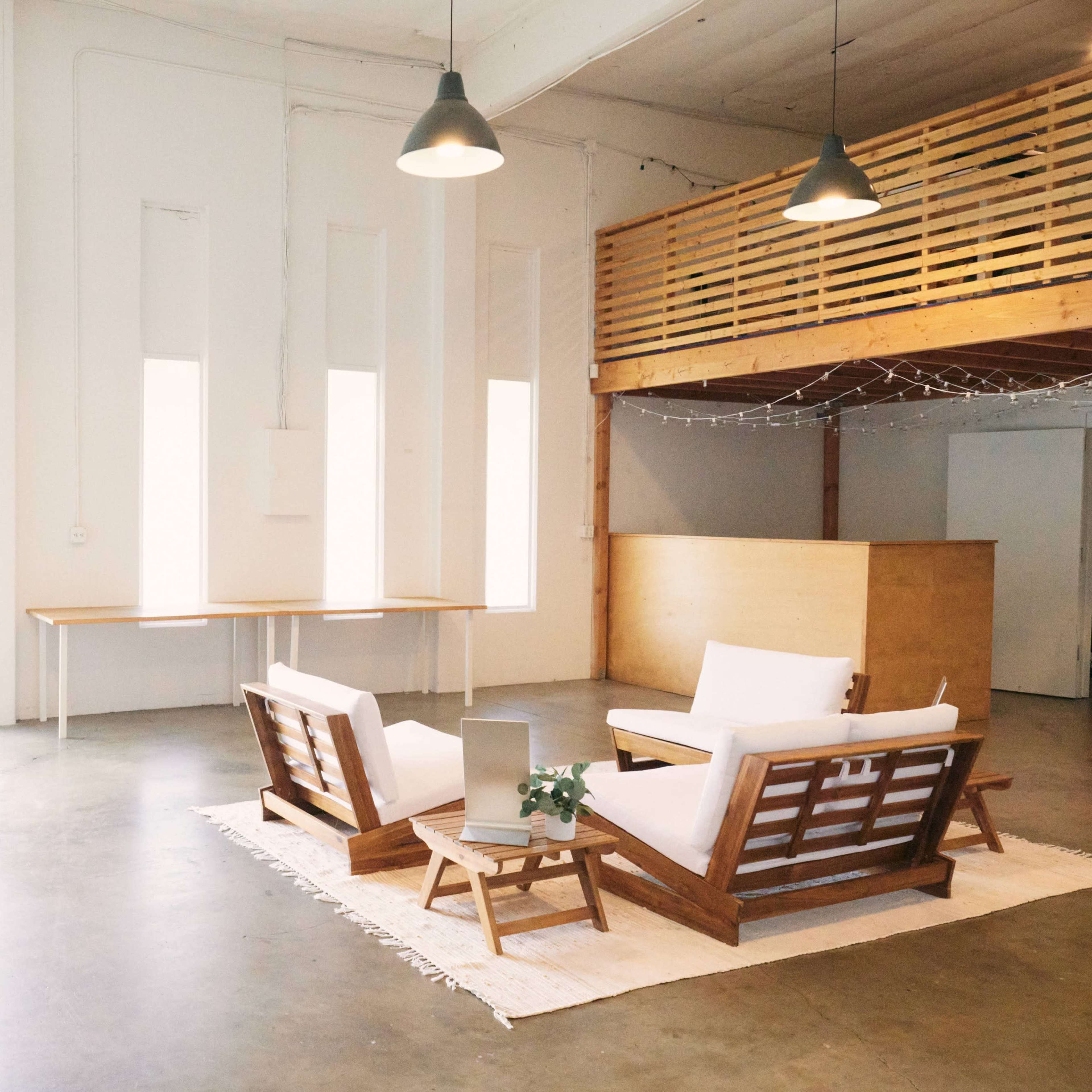 A spacious, modern interior with a seating area featuring wooden furniture, a small table, and a loft area in the background.
