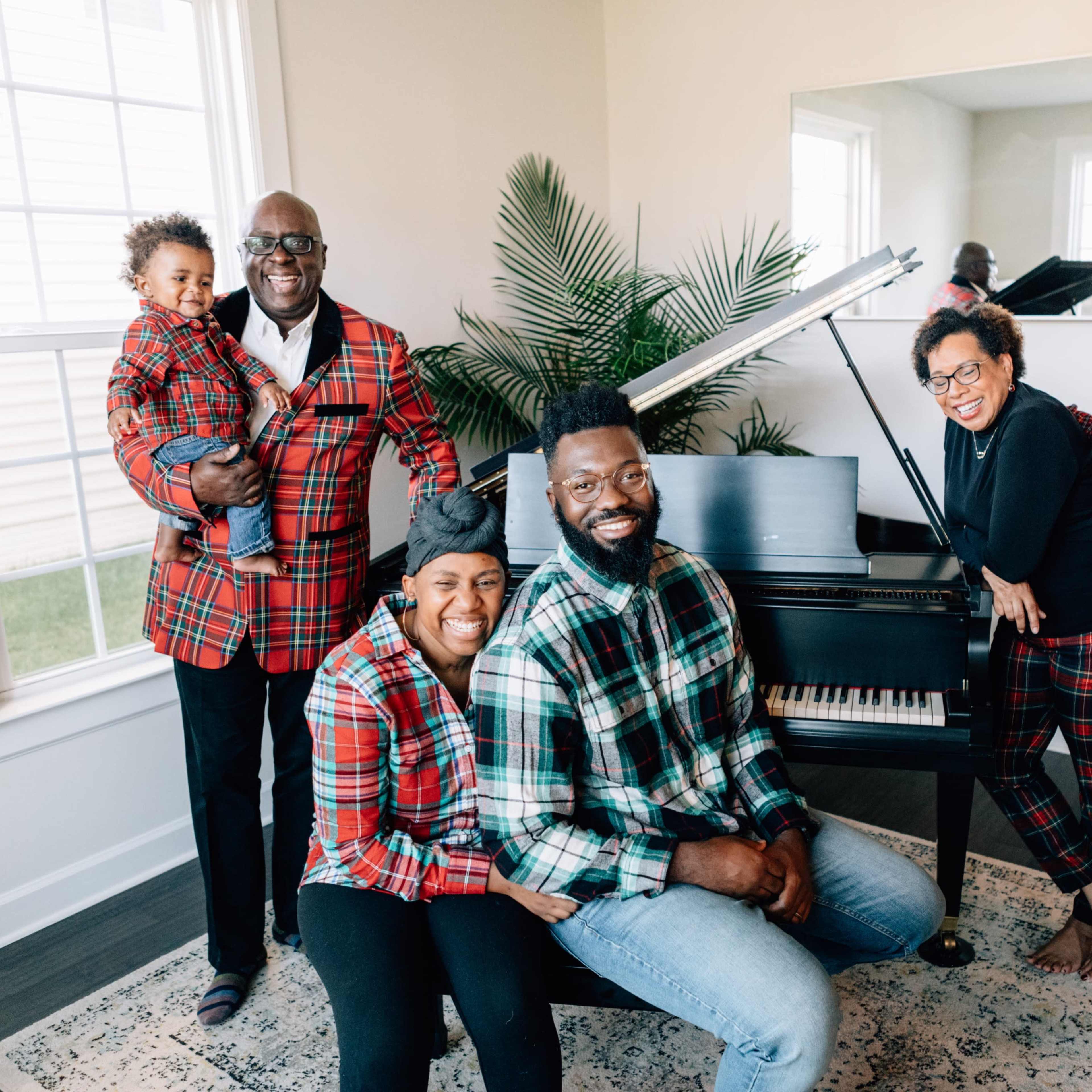 A family poses together in a bright room with a piano, wearing matching plaid outfits.