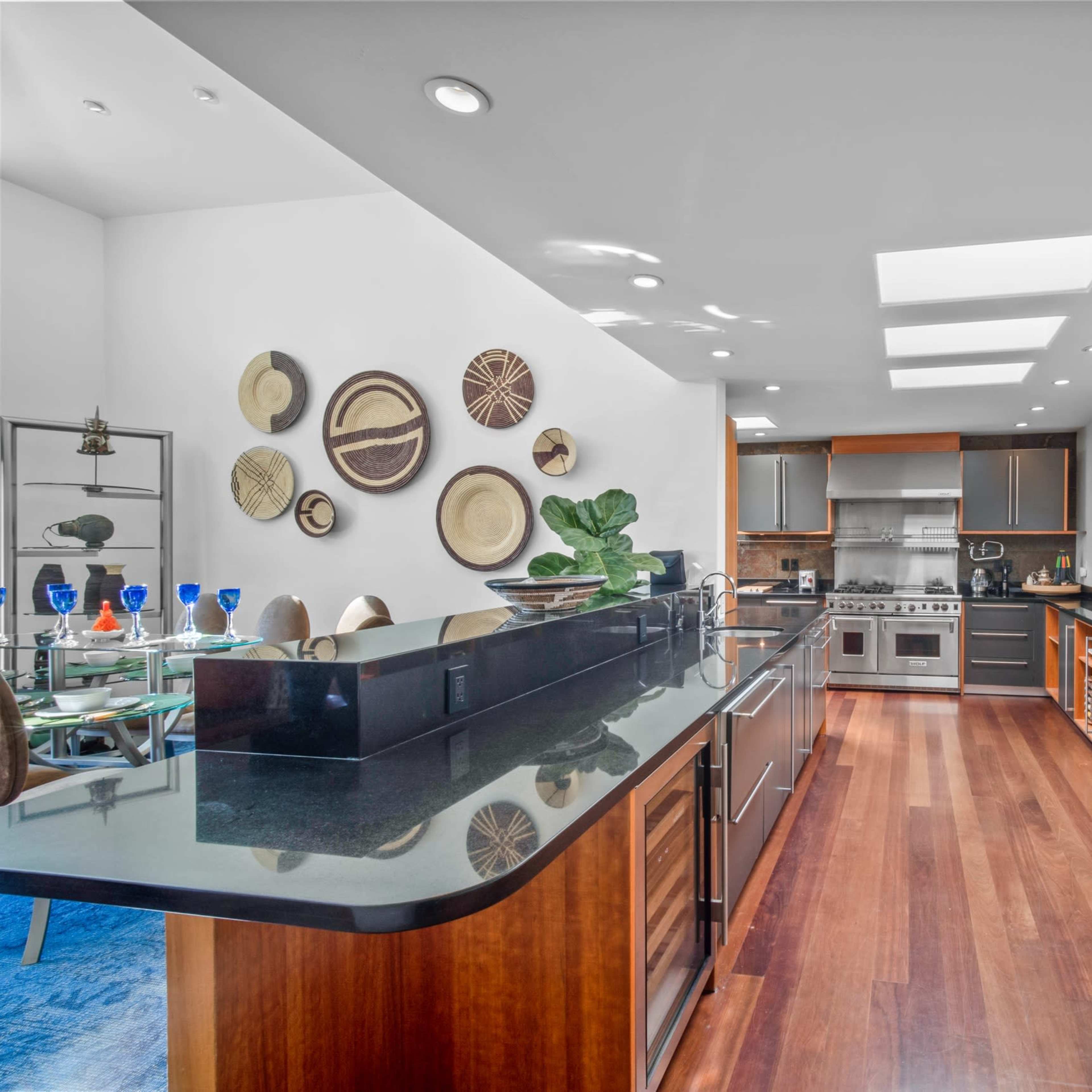 The kitchen features modern appliances, dark countertops, and wooden cabinetry, with a dining area visible in the background.