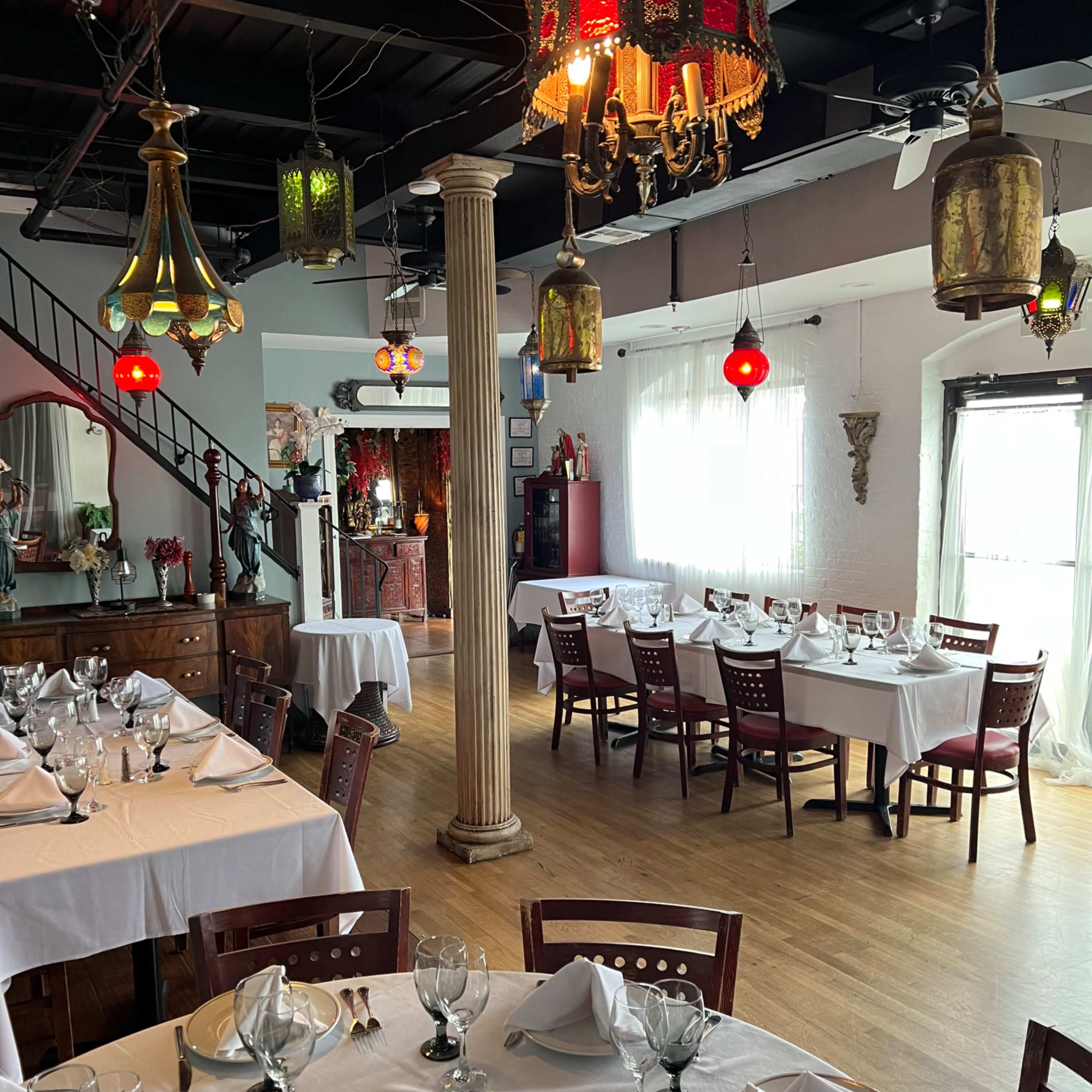 A dining area of a restaurant featuring table settings with white linens, glassware, and a mix of hanging lanterns and decorative elements.