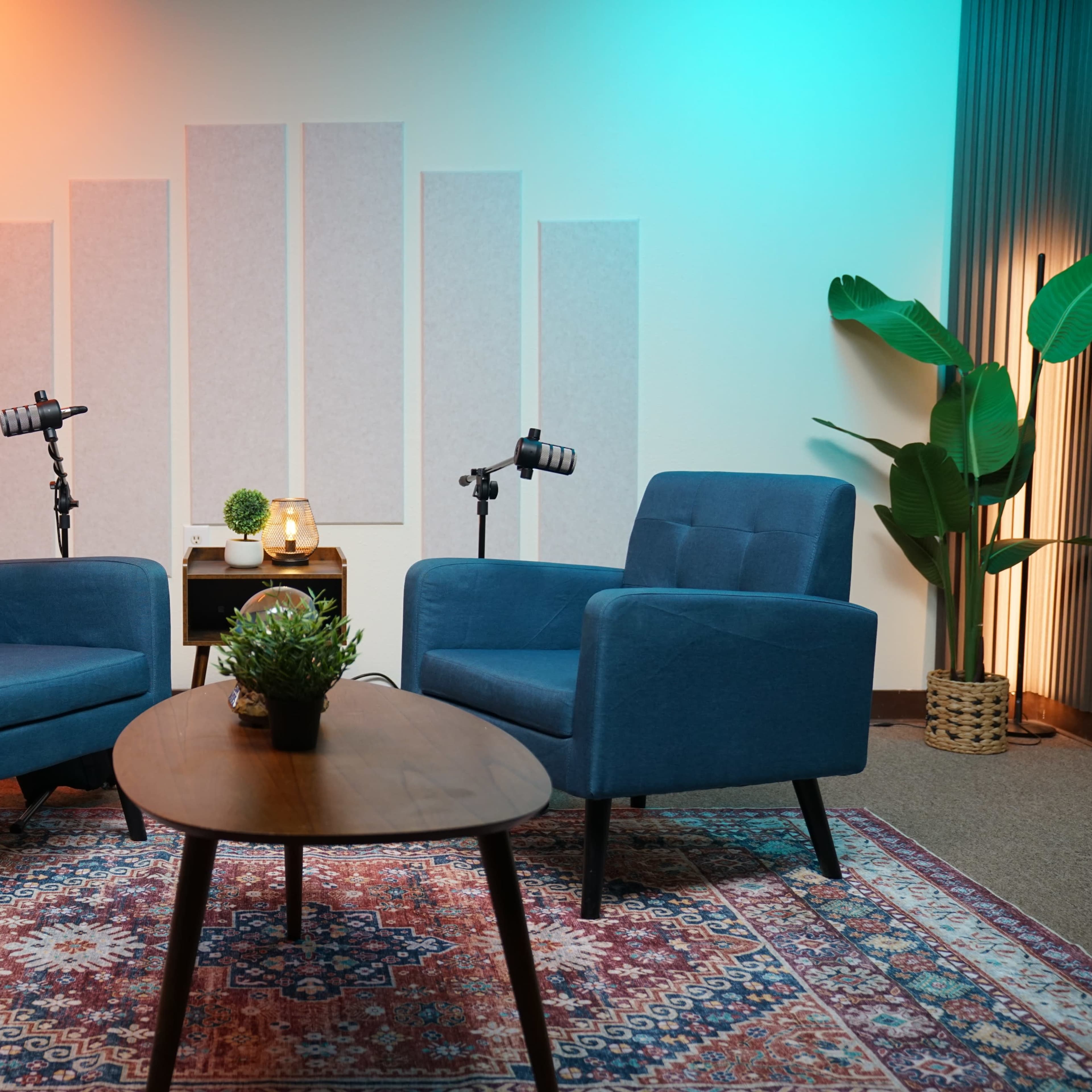A cozy interview setup featuring two blue chairs, a small table with decorative items, and plants, all under soft, colored lighting.