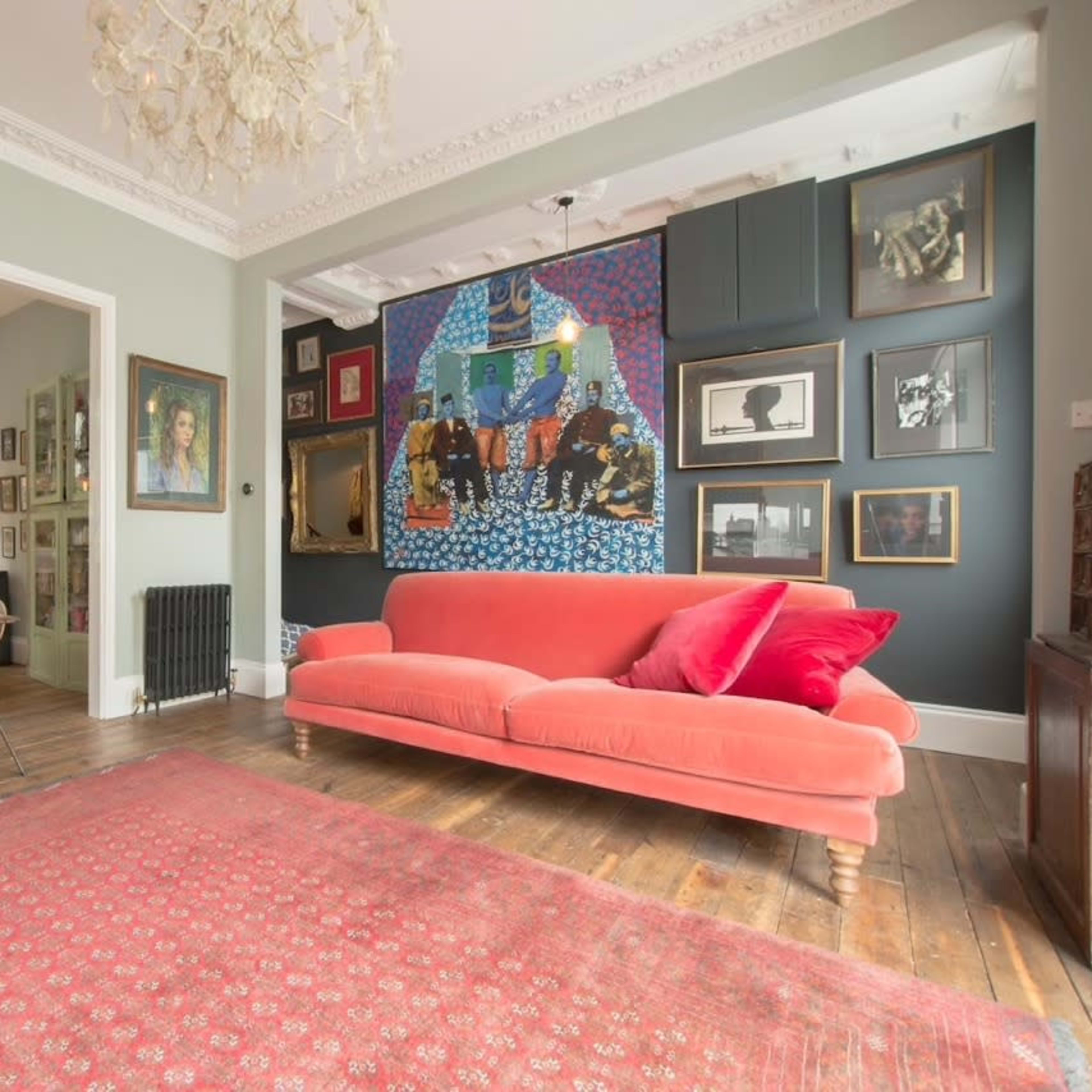 A spacious living area featuring a red velvet sofa, an intricately patterned rug, and a gallery wall with various framed artworks.
