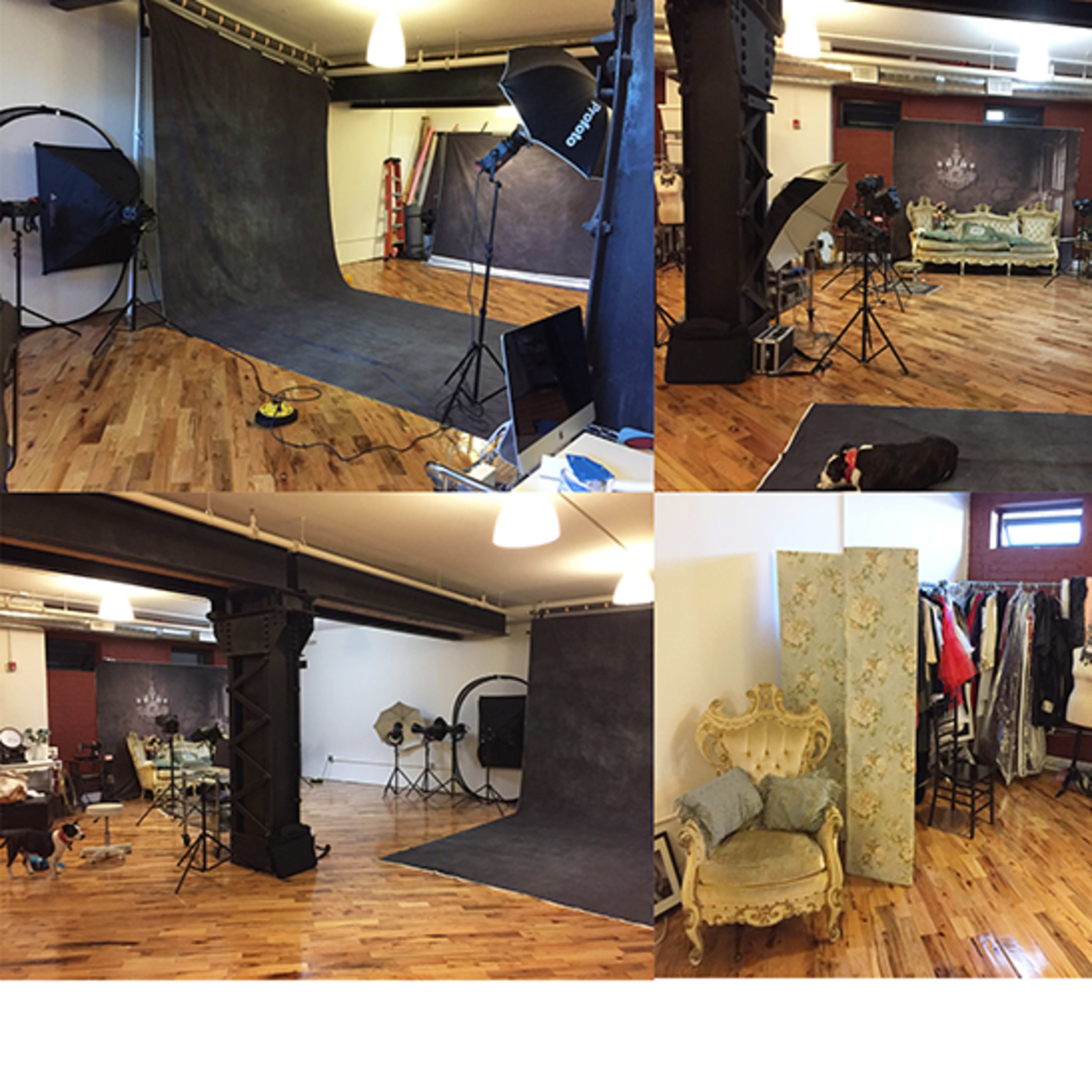 A photography studio featuring a variety of backdrops, lighting equipment, and vintage furniture arranged in a spacious wooden-floored room.