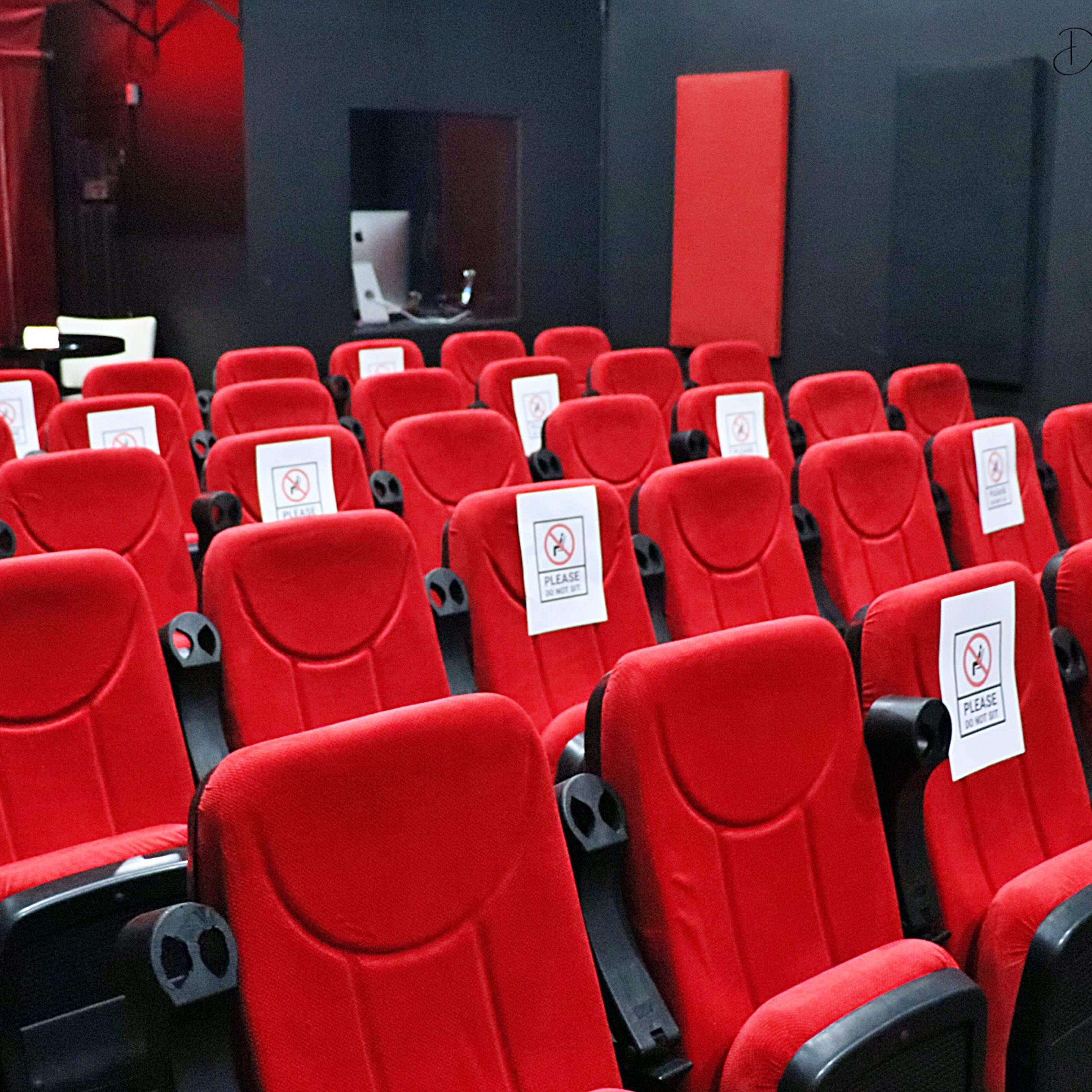 An empty movie theater is filled with red seats, each marked with a sign indicating they are not to be used.