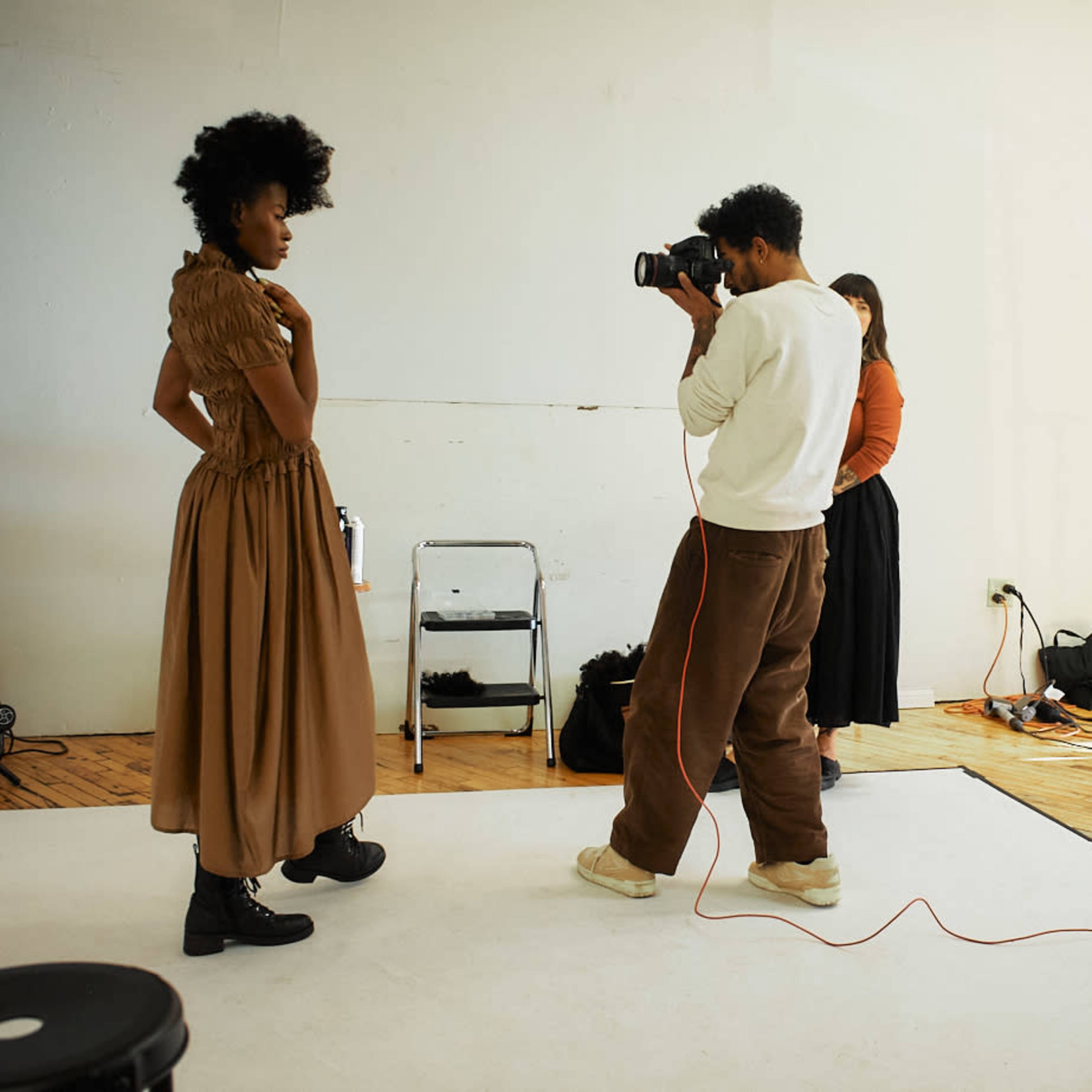A photographer captures an image of a model wearing a long dress in a studio setting while two people observe.
