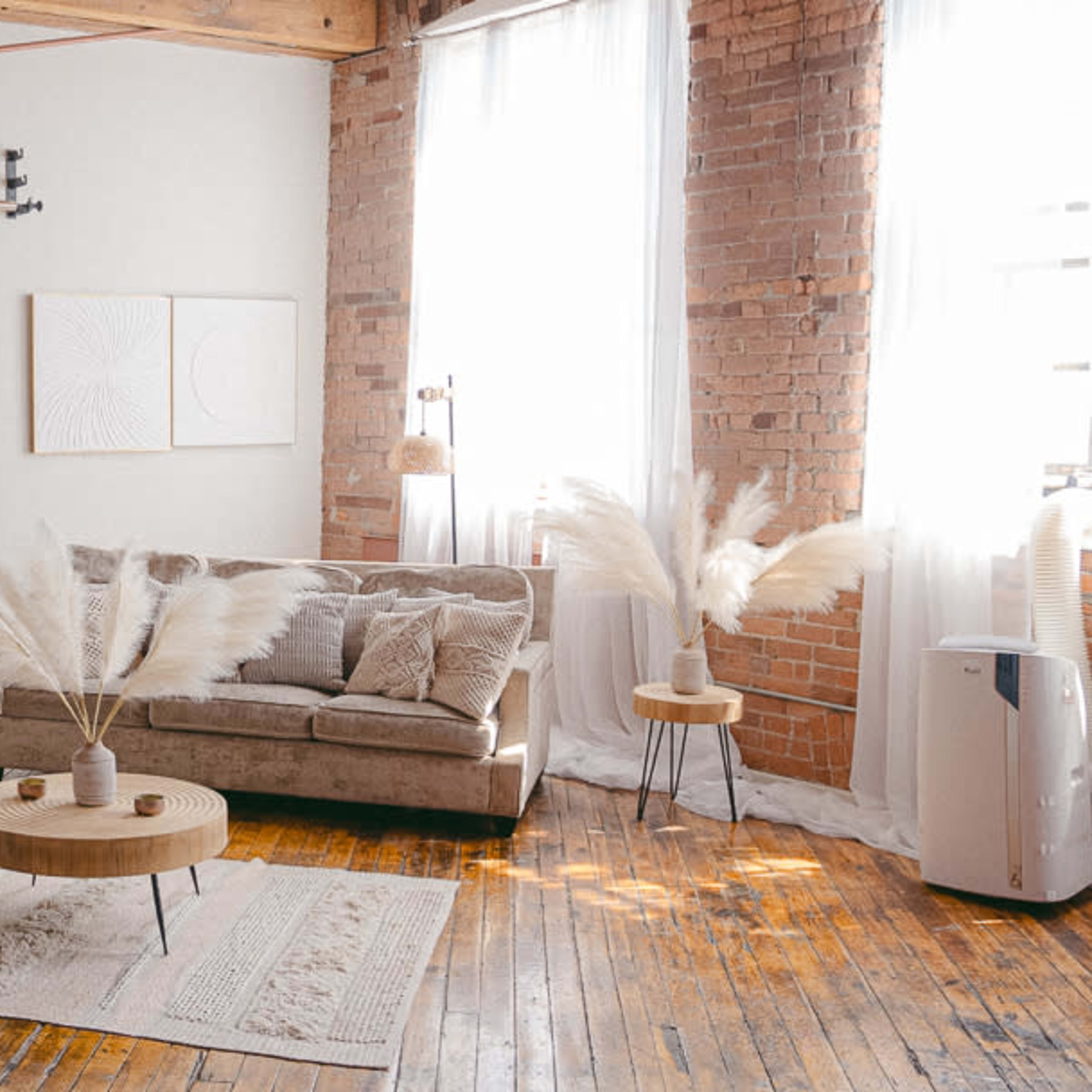 A bright room with a sofa, two small tables, and decorative elements, all set against a backdrop of exposed brick walls and large windows.