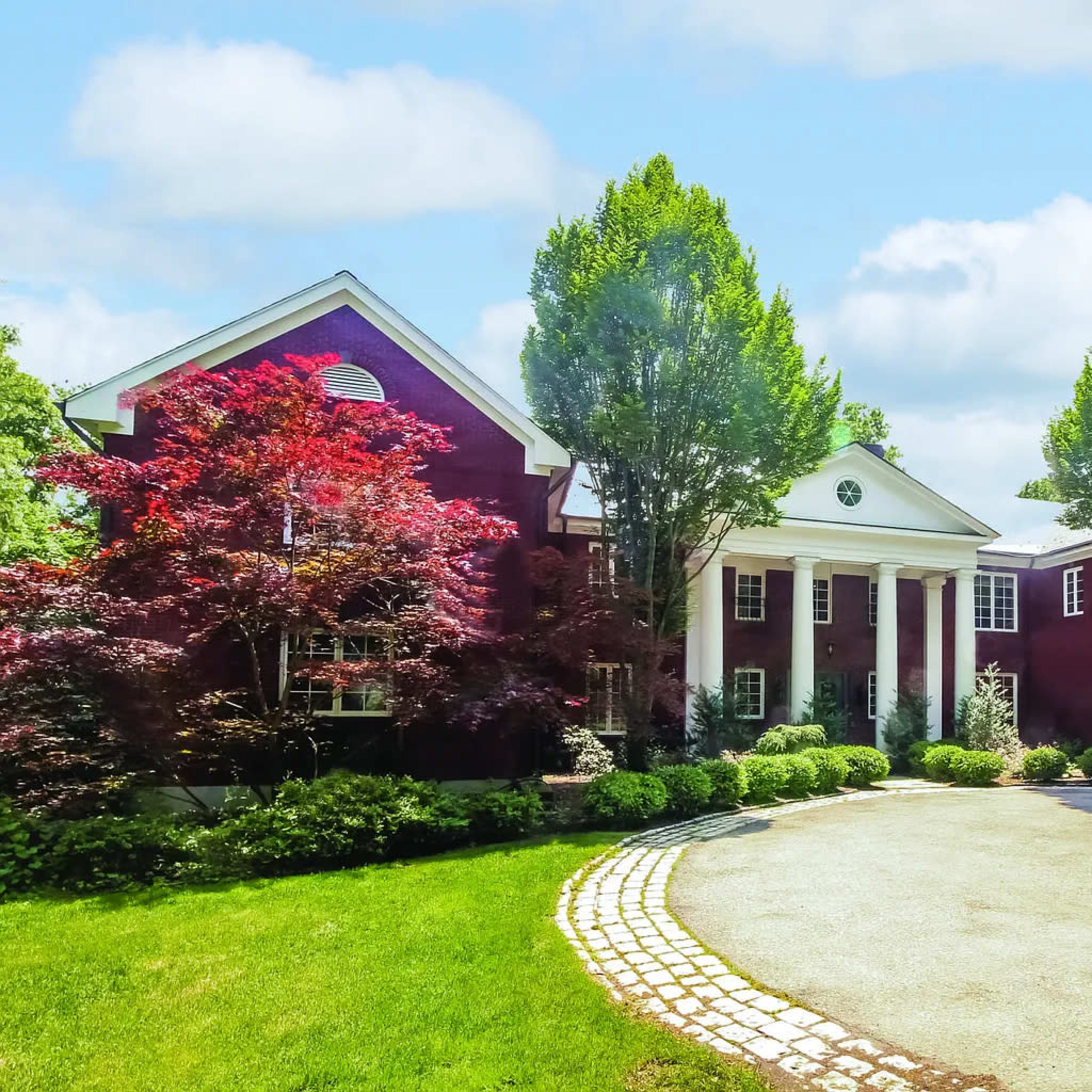 A large, red brick house with white columns, surrounded by greenery and a circular driveway.