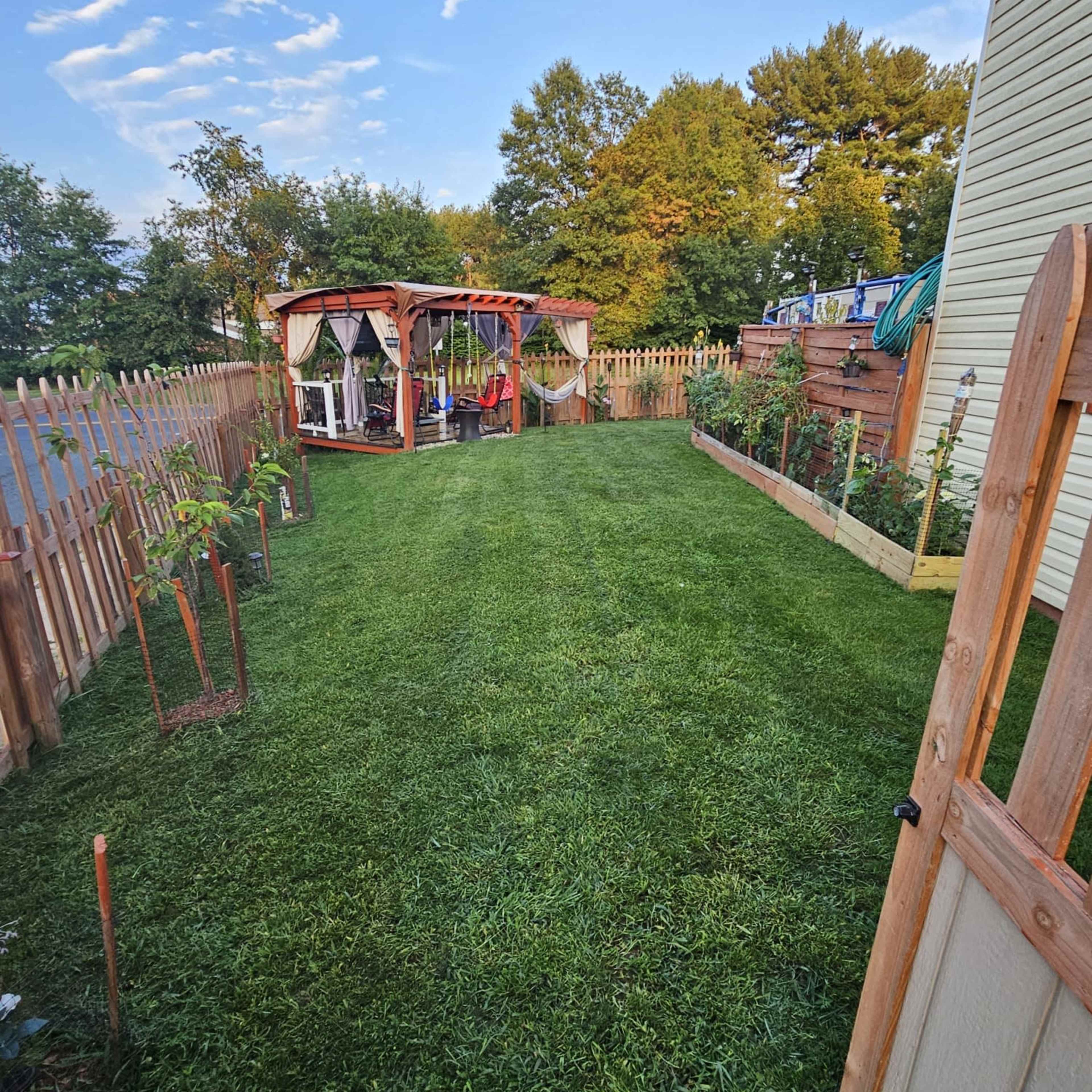 A well-maintained backyard features a grassy area, a wooden gazebo at the far end, and a fence surrounding the space.