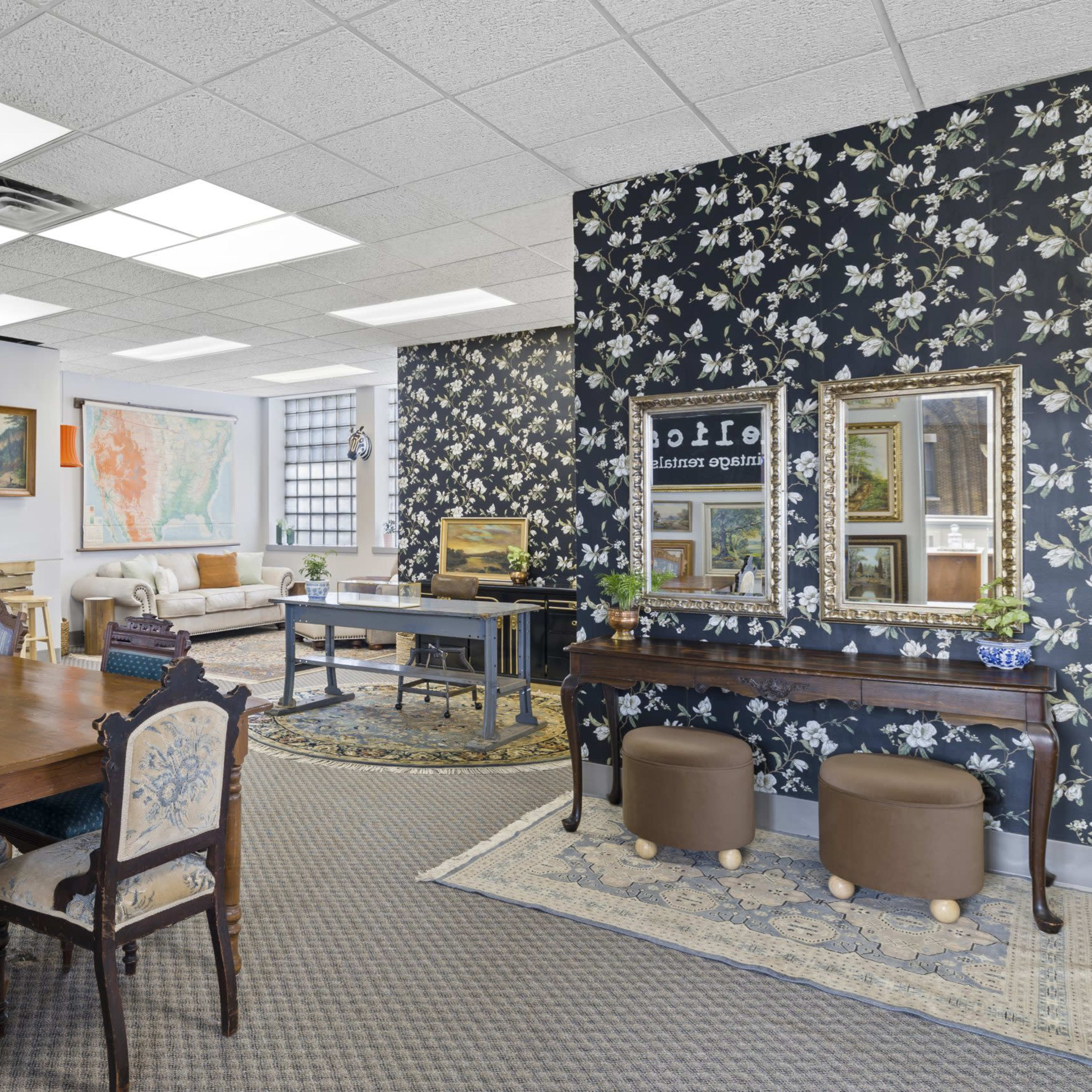 A spacious office area featuring a dining table with chairs, a seating area with a couch, and decorative floral wallpaper.
