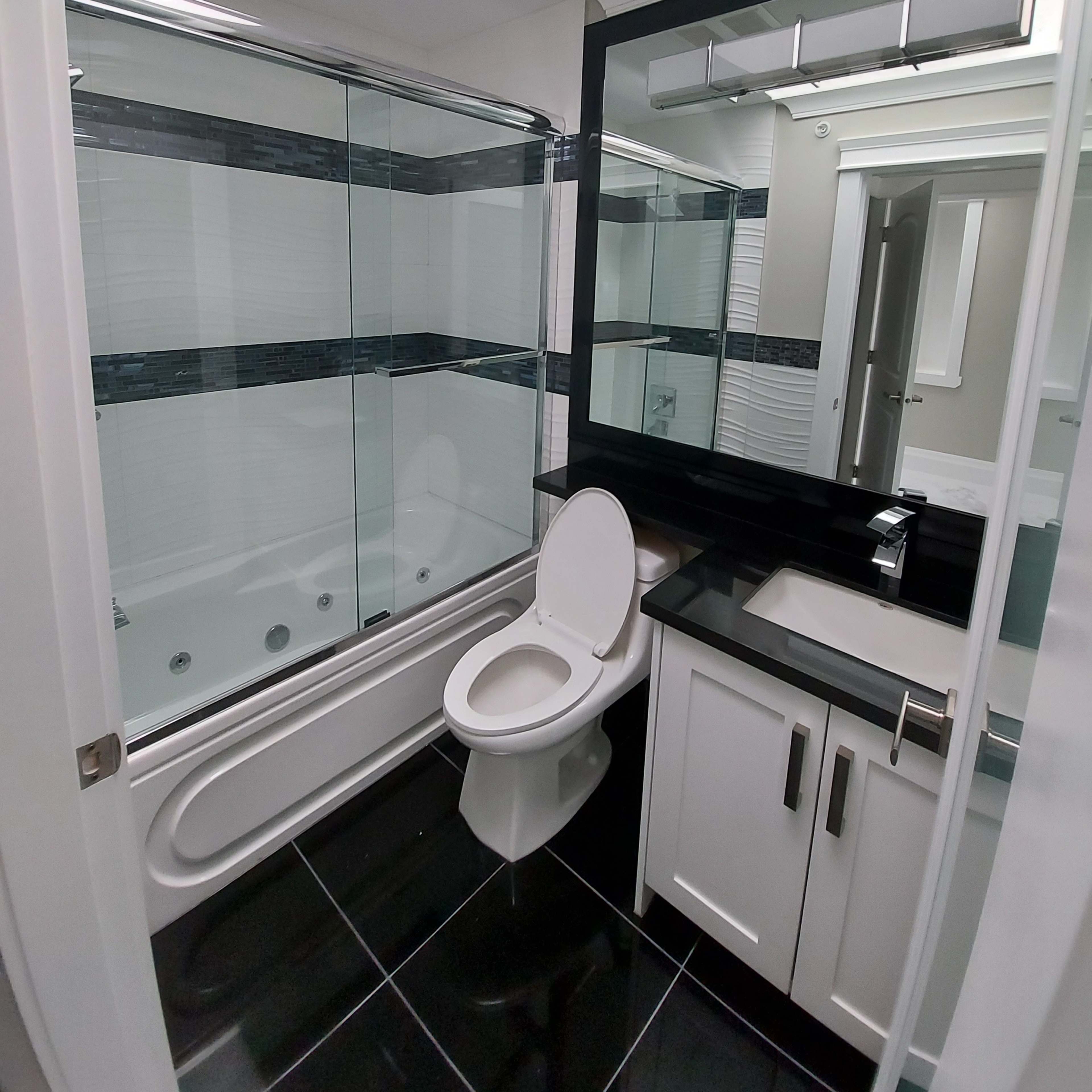 A modern bathroom featuring a bathtub with a glass enclosure, a toilet, and a sink with a mirror above it.