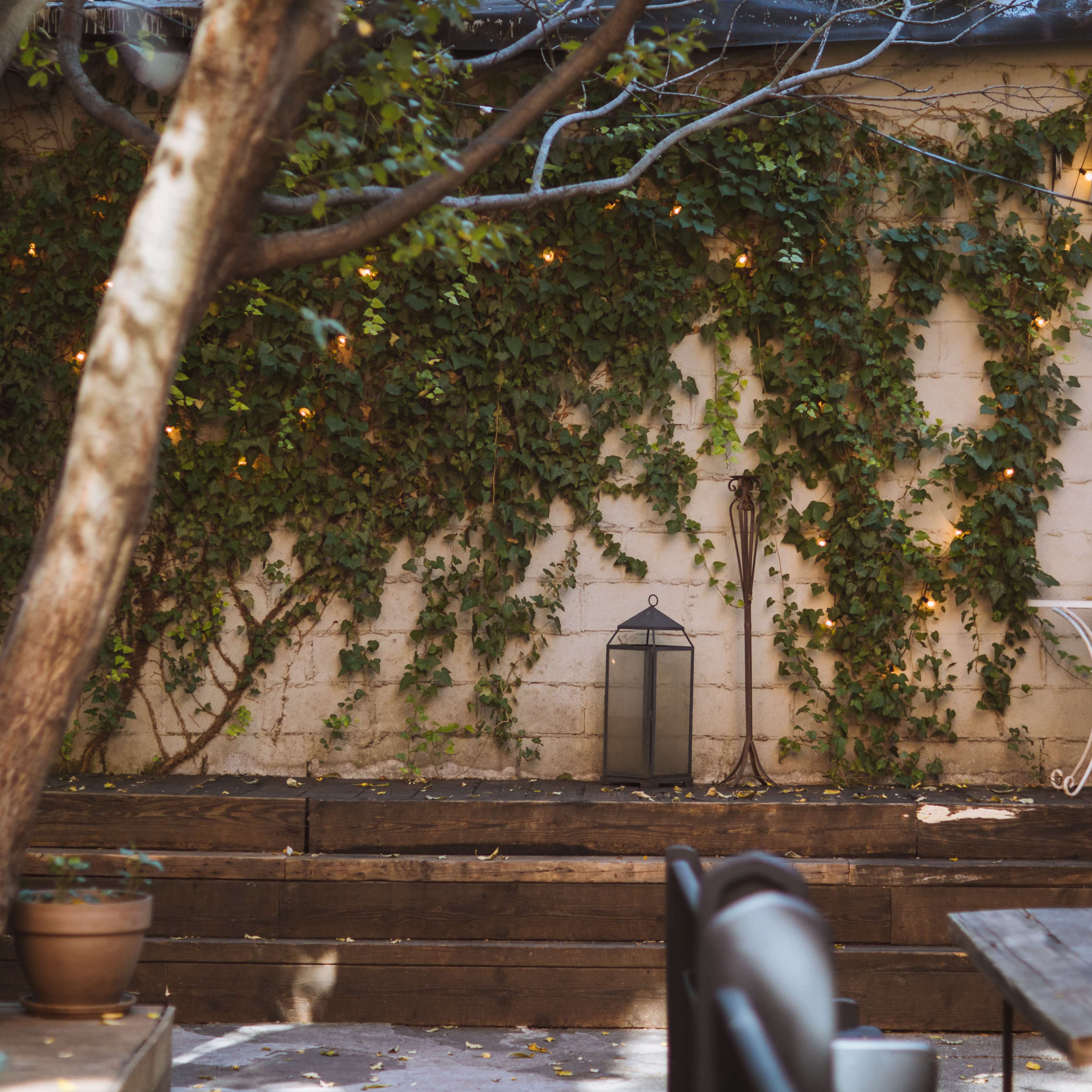 A garden area features wooden decking, a small white table with a chair, a lantern, and an ivy-covered stone wall.
