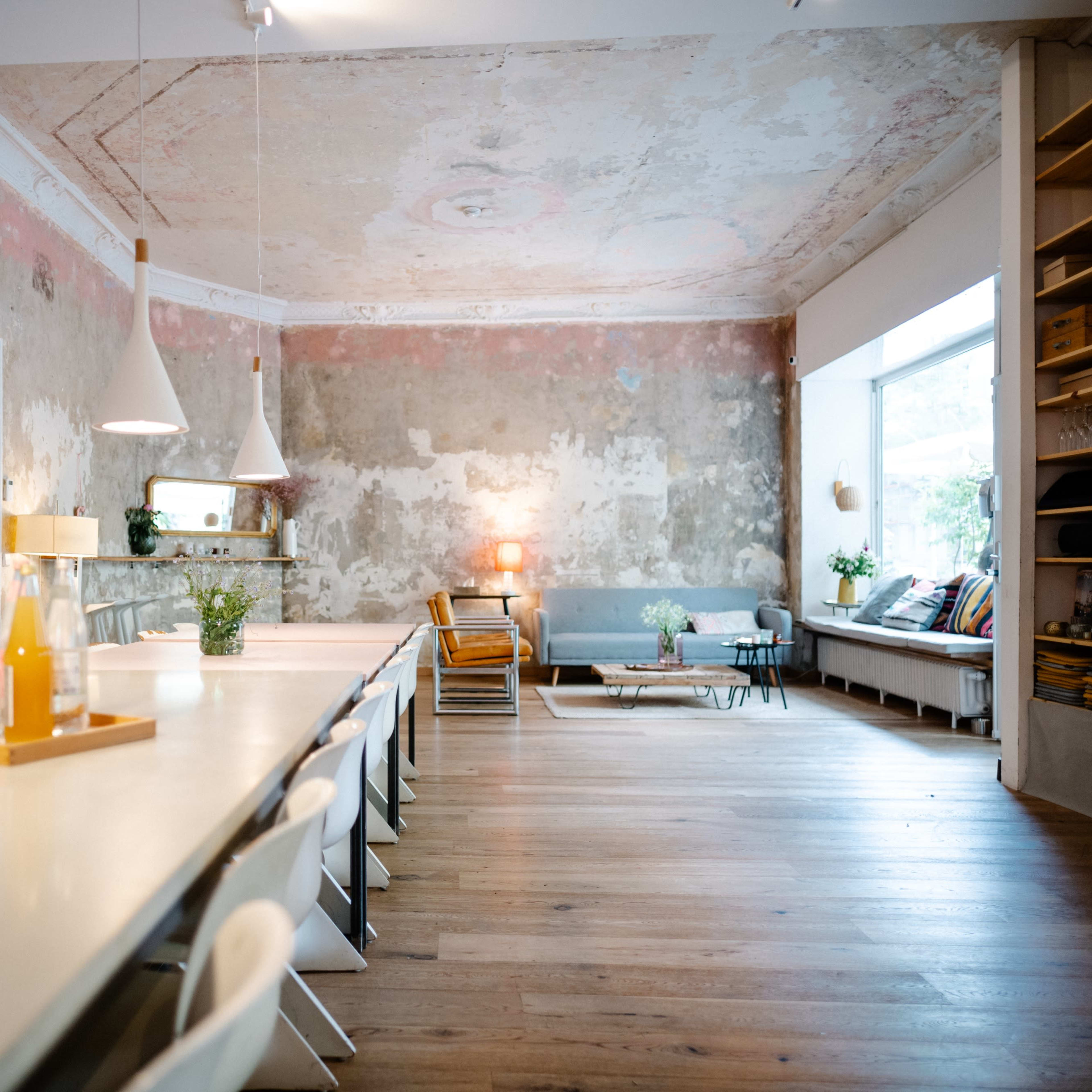 A spacious, modern dining area with a long white table, white chairs, and exposed brick walls, complemented by natural light from a large window.
