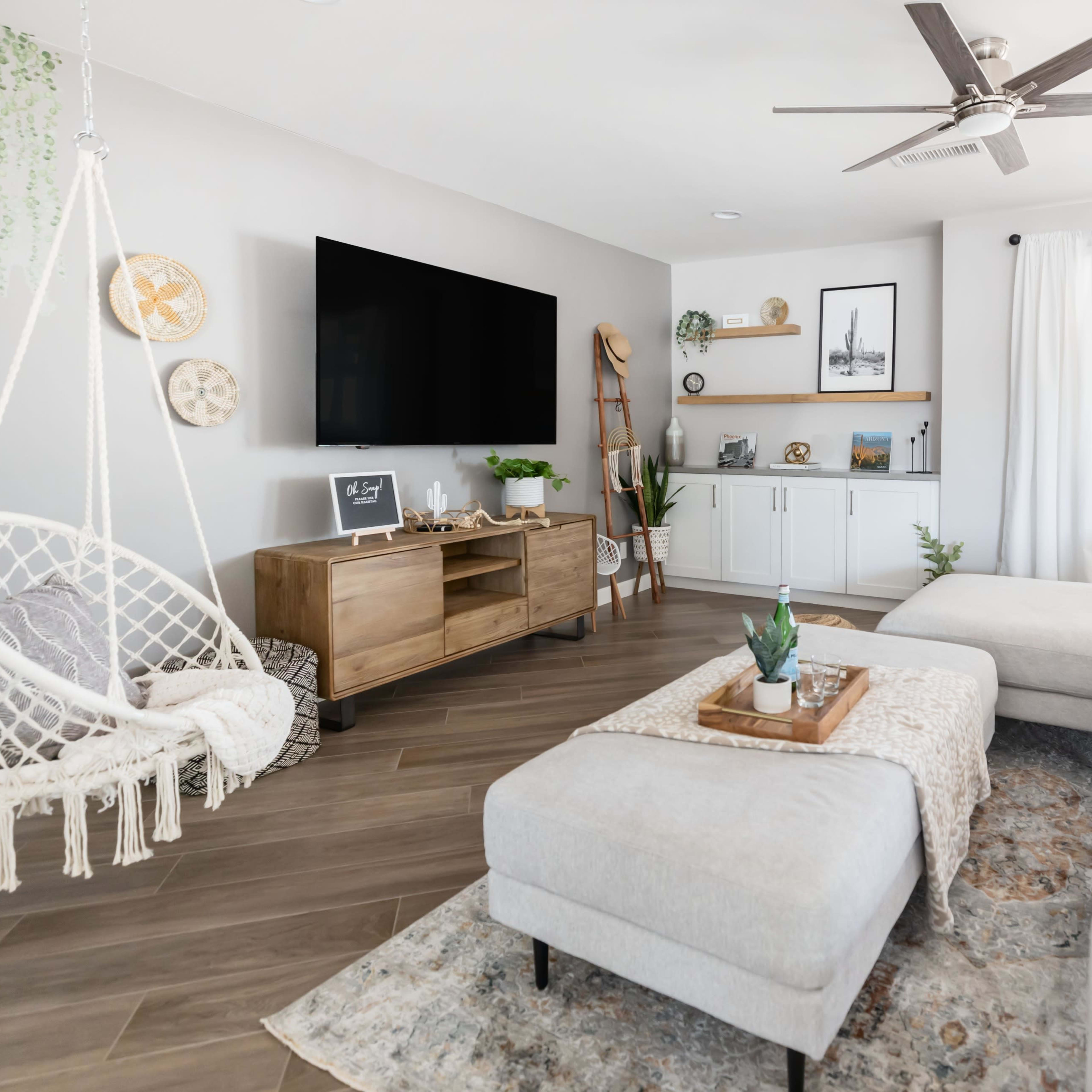 A modern living room with a white sectional sofa, a hanging chair, a wooden TV stand, and a coffee table decorated with a plant and a tray.