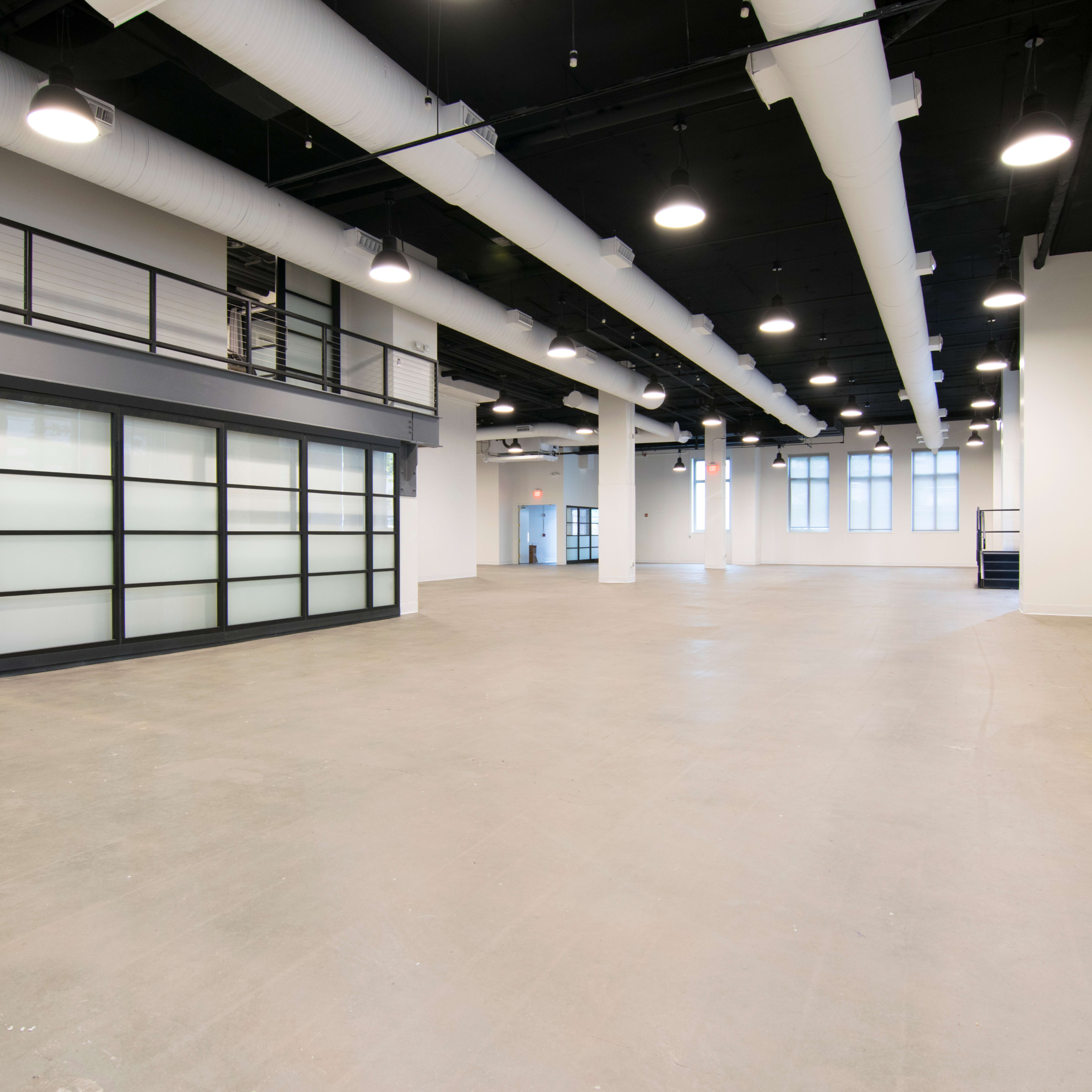 A spacious, empty commercial interior with high ceilings, large windows, and a mezzanine level.