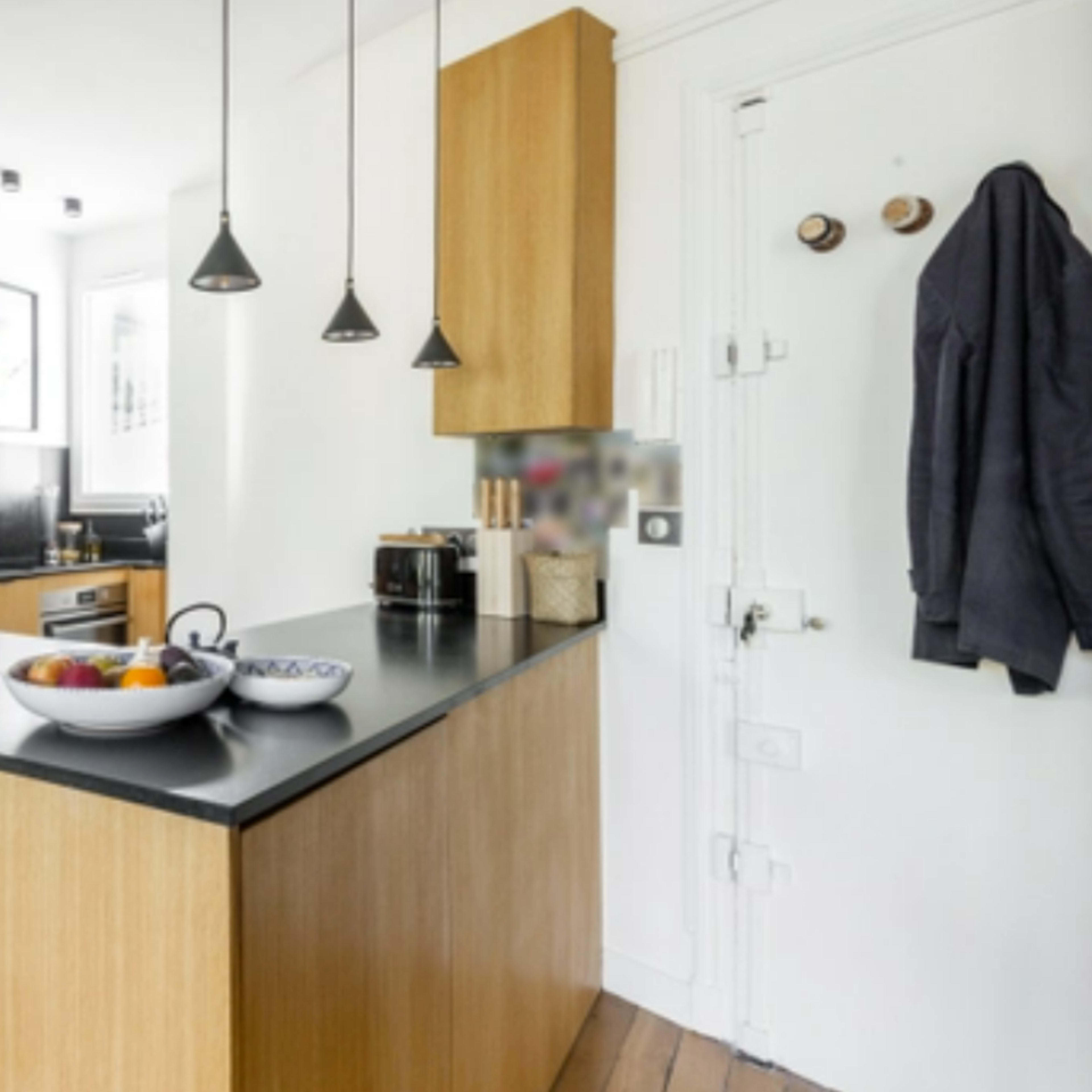 A modern kitchen featuring a wooden island with a black countertop, pendant lights, and a bowl of fruit on the surface.