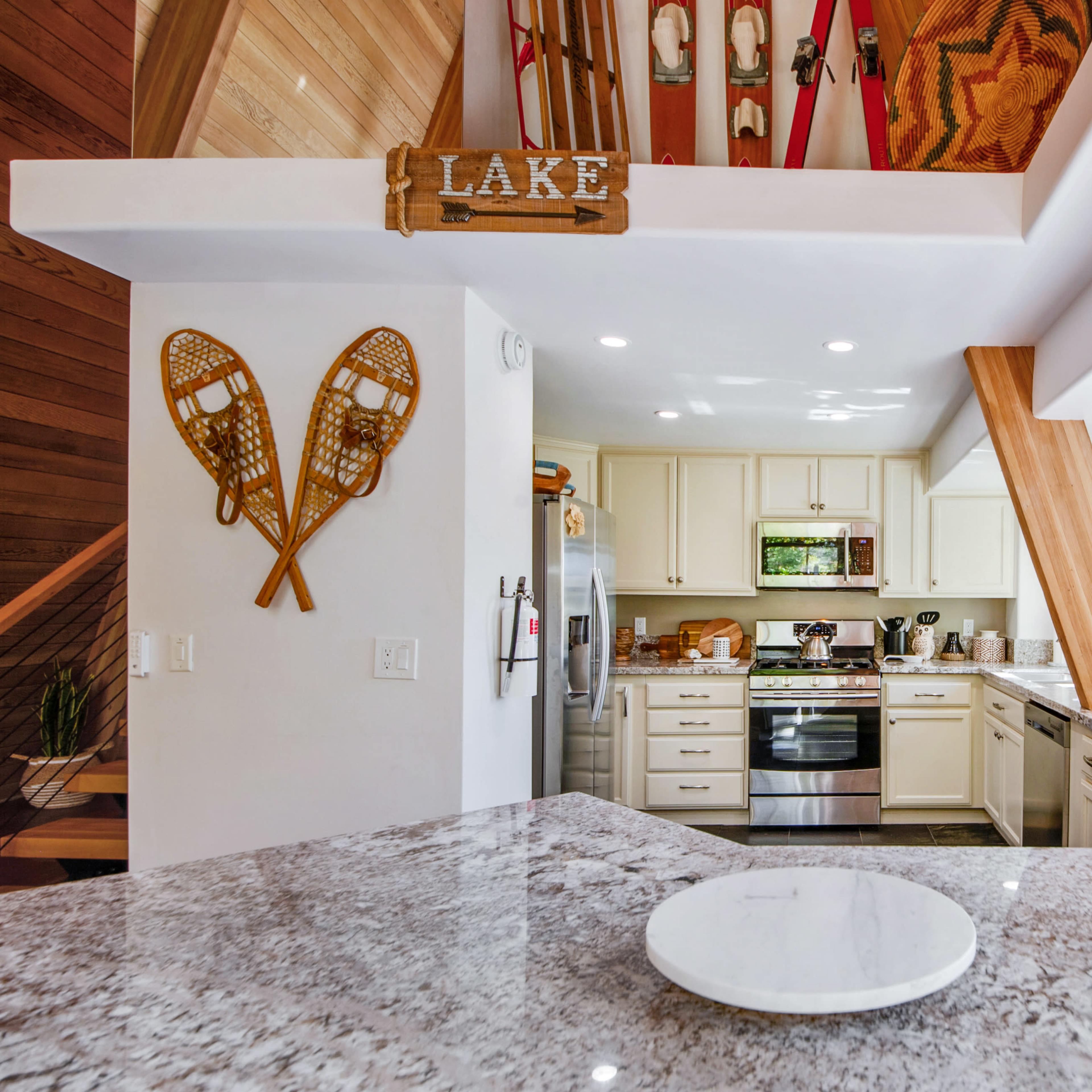 A modern kitchen with light-colored cabinetry, a large granite countertop, and wooden accents, featuring snowshoes decor and a view of trees outside.