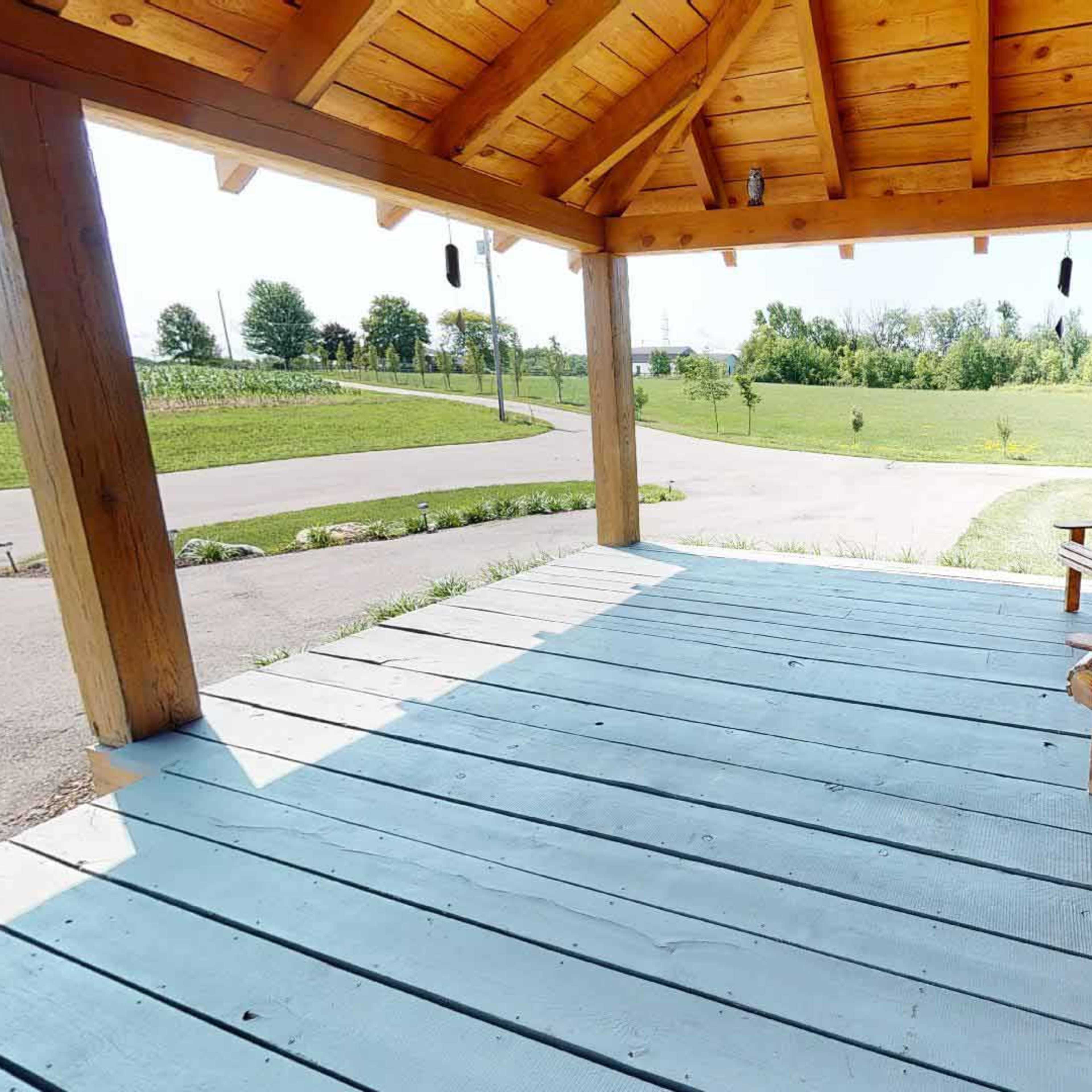 A wooden porch features two chairs and overlooks a grassy landscape with trees in the distance.