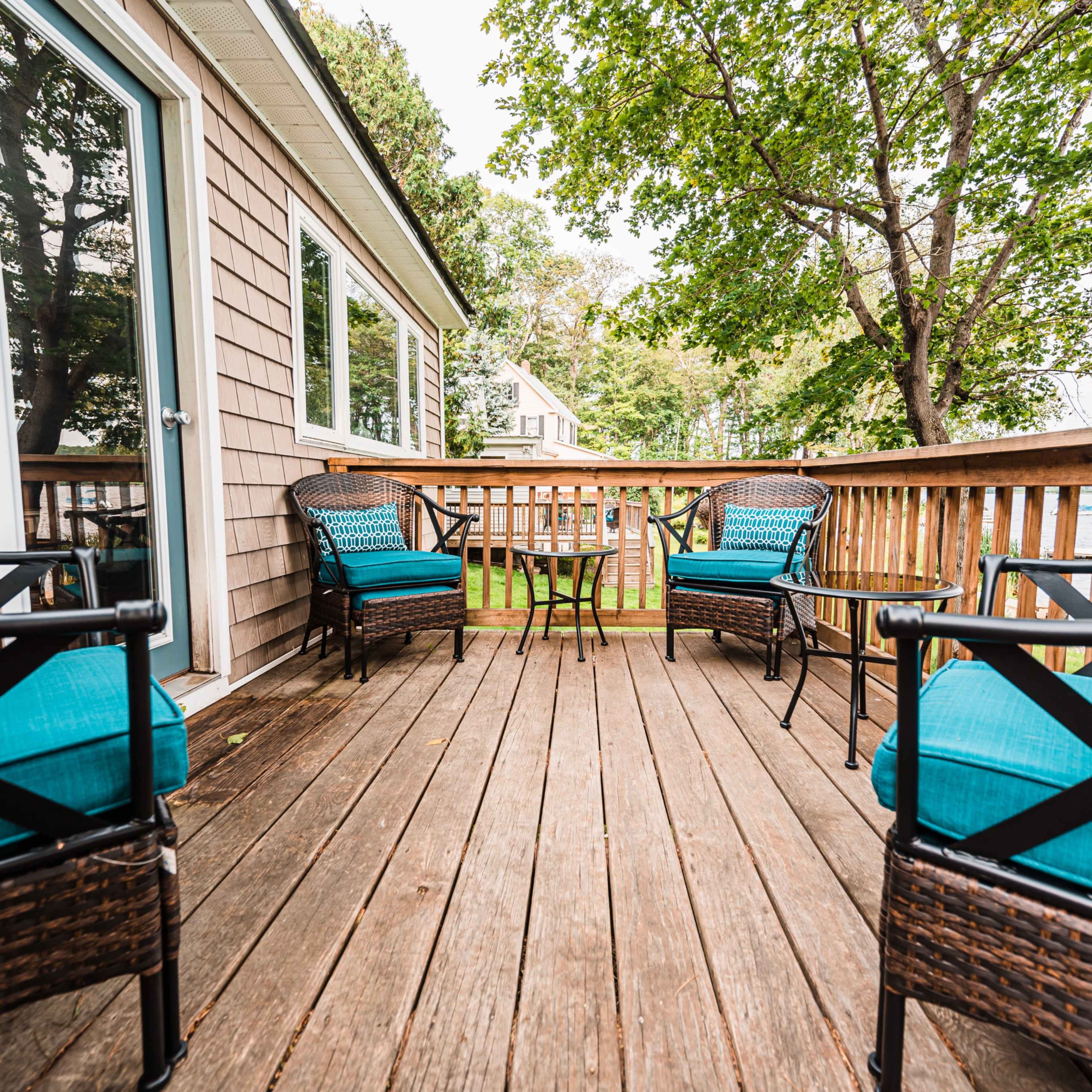 A wooden deck area with four wicker chairs featuring turquoise cushions and a small table in the center.
