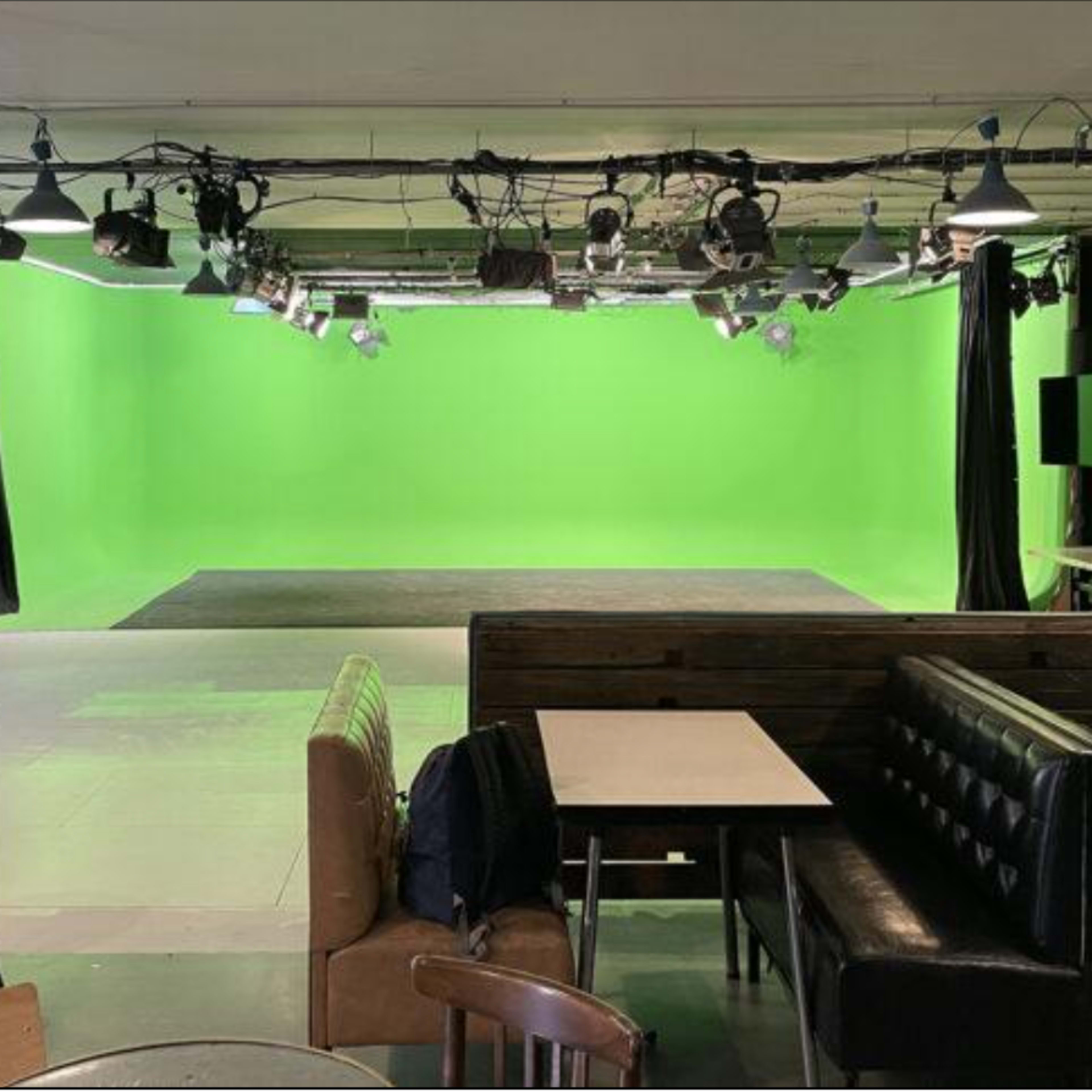 A studio space with a green screen backdrop, surrounded by various seating arrangements and lighting fixtures.