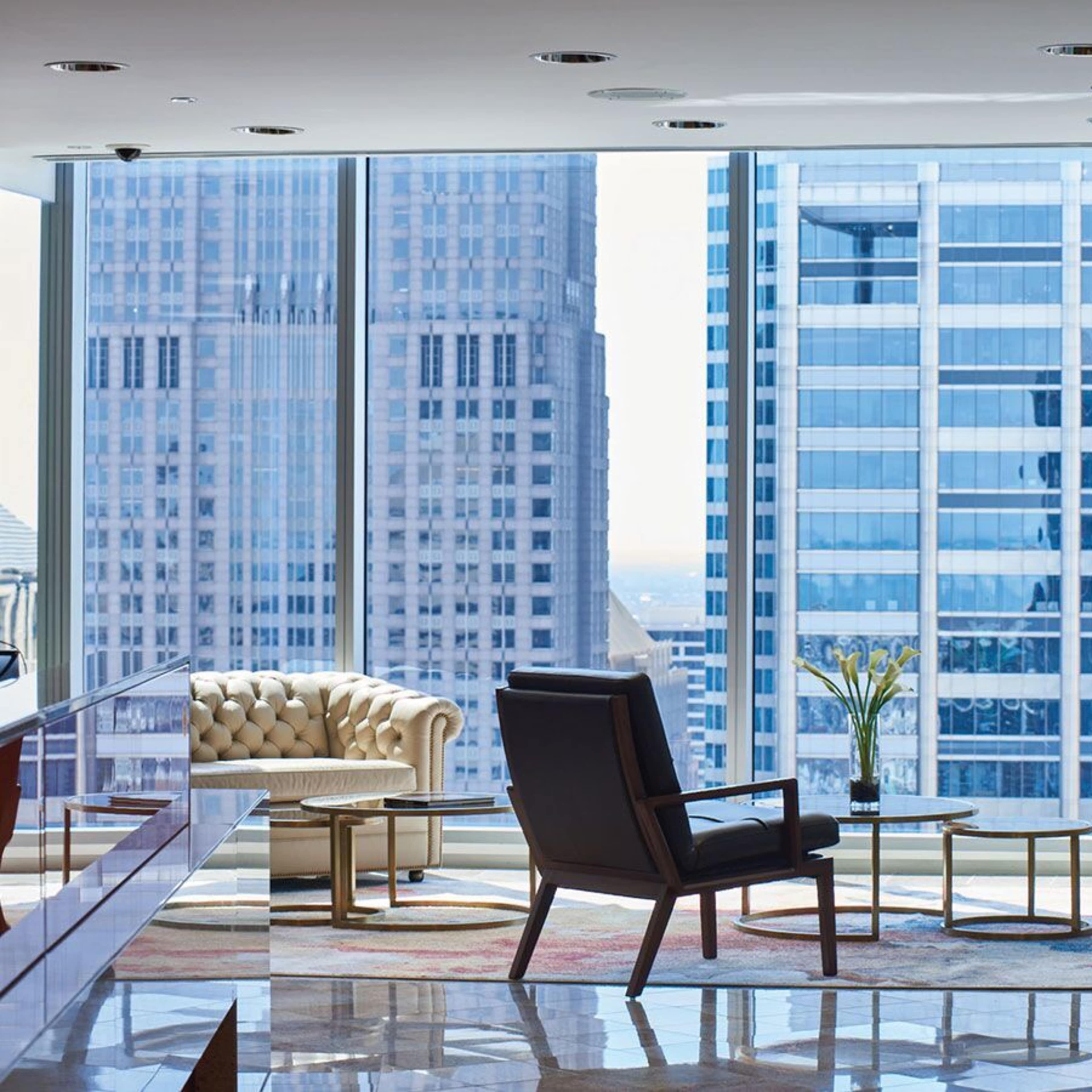 A man sits in a modern office lounge area with large windows overlooking a cityscape.