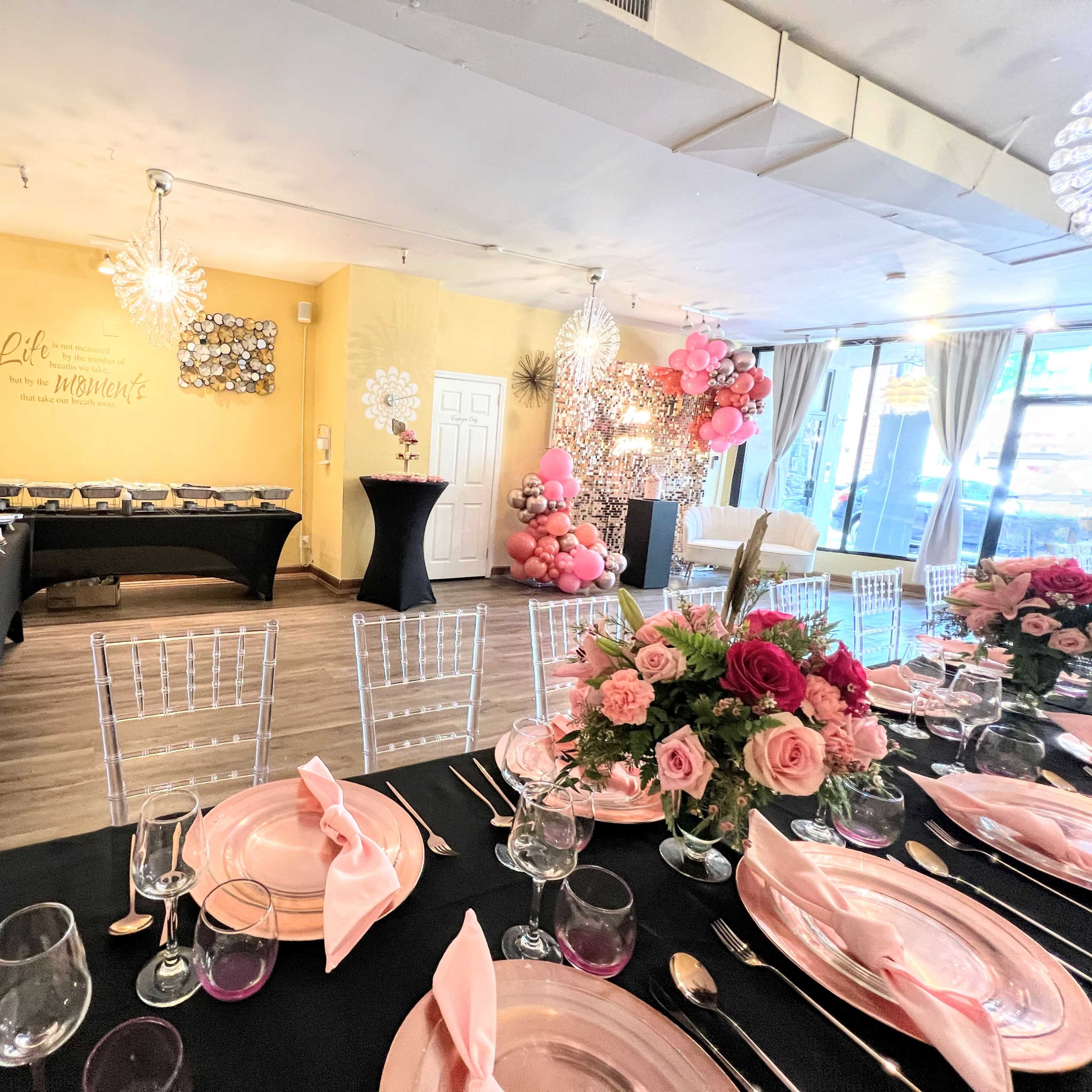 An elegantly decorated dining room with a black table, pink table settings, and a decorated buffet area in the background.