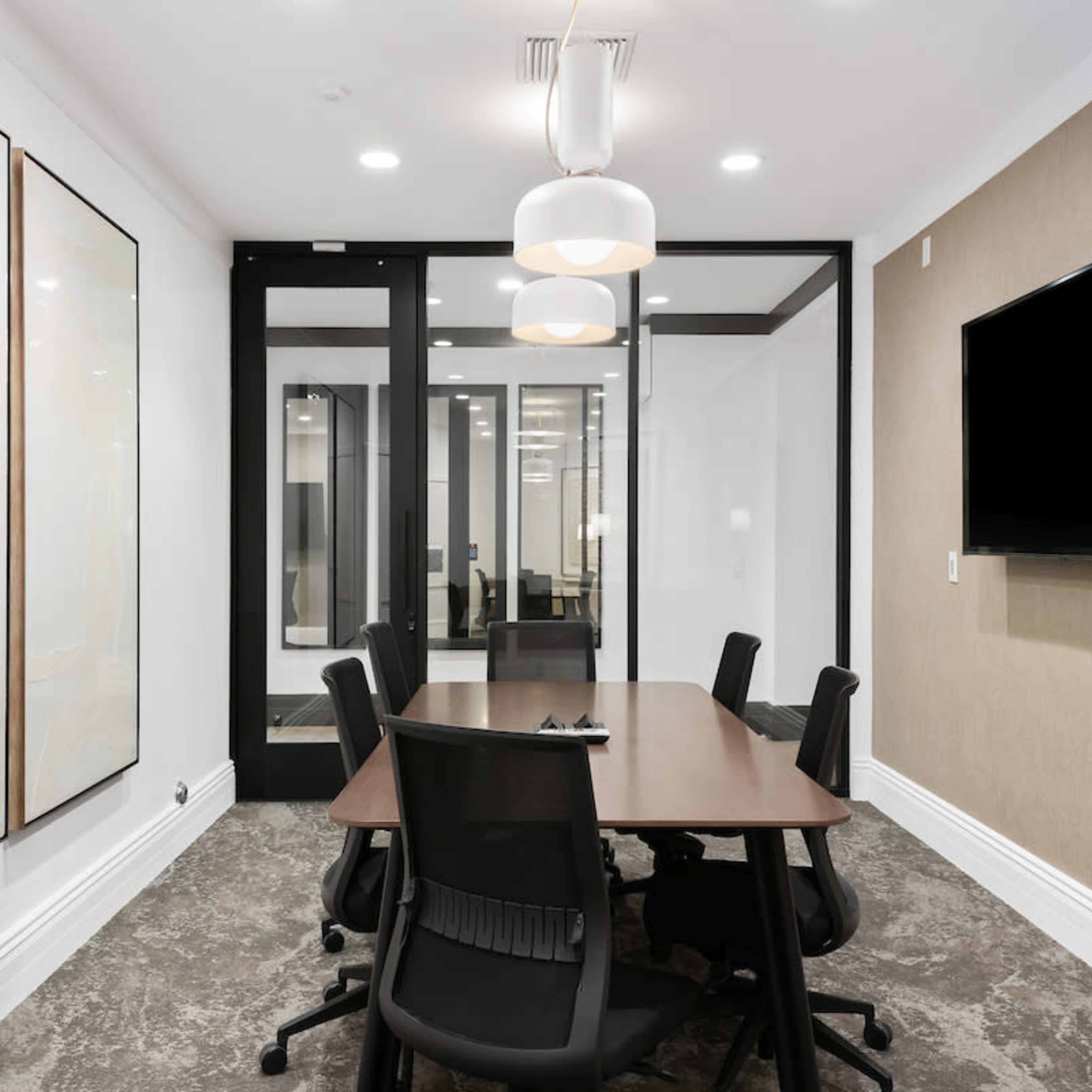 A modern conference room with a rectangular table, black chairs, and a large wall-mounted television.