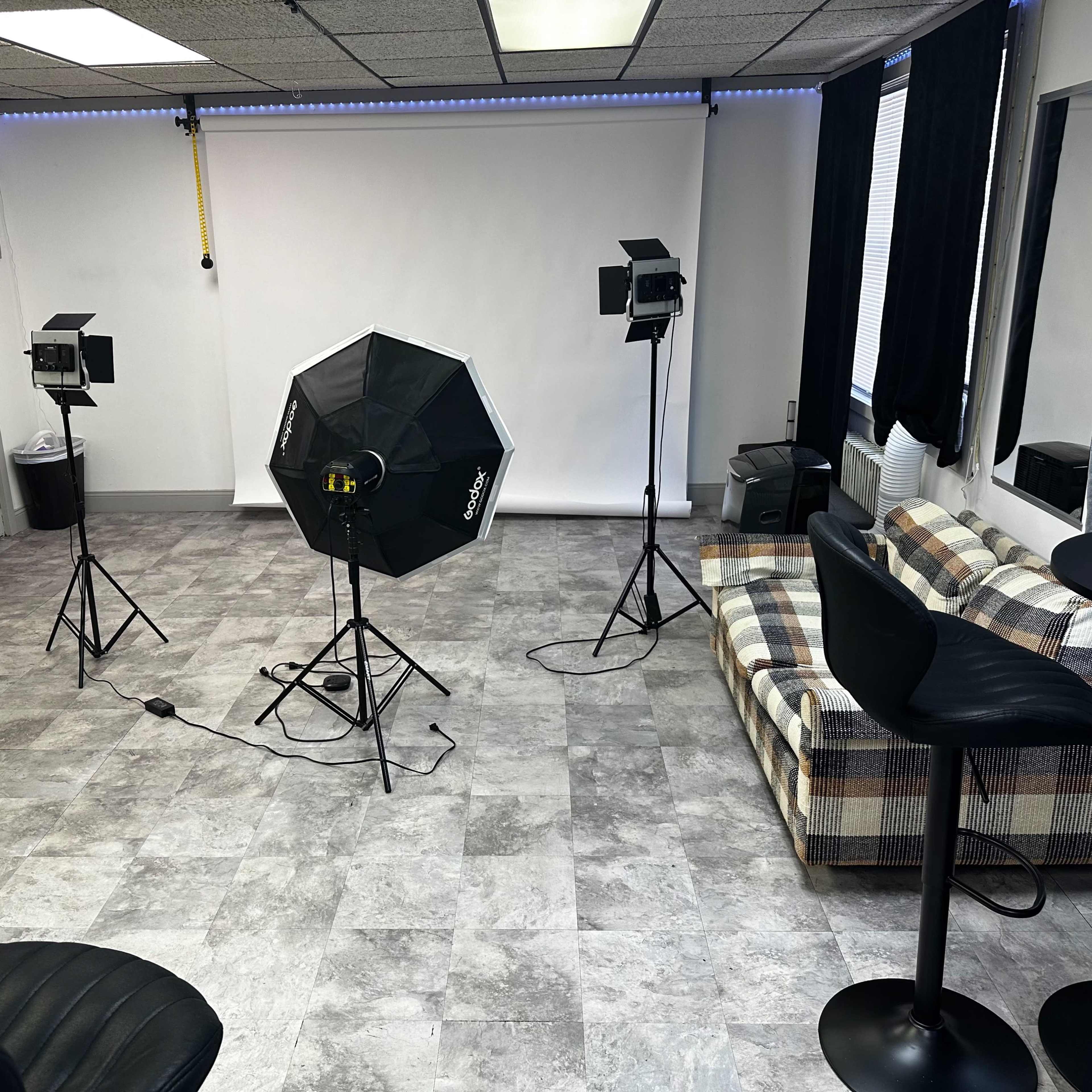 A photography studio setup with lighting equipment, a checkered sofa, and a small bar table.