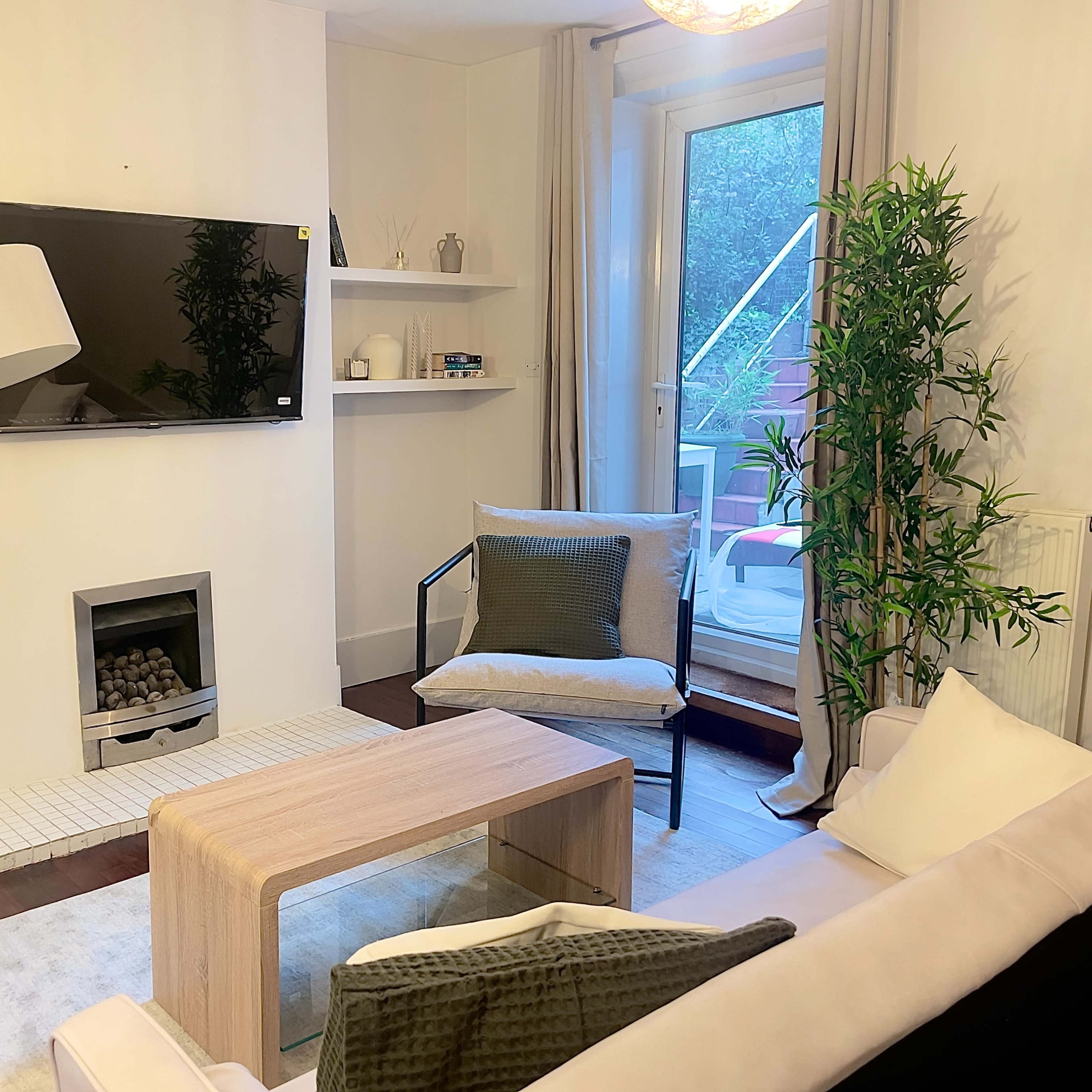 A modern living room features a television mounted on the wall, a floor lamp, a glass coffee table, and a sliding door that opens to a small balcony.