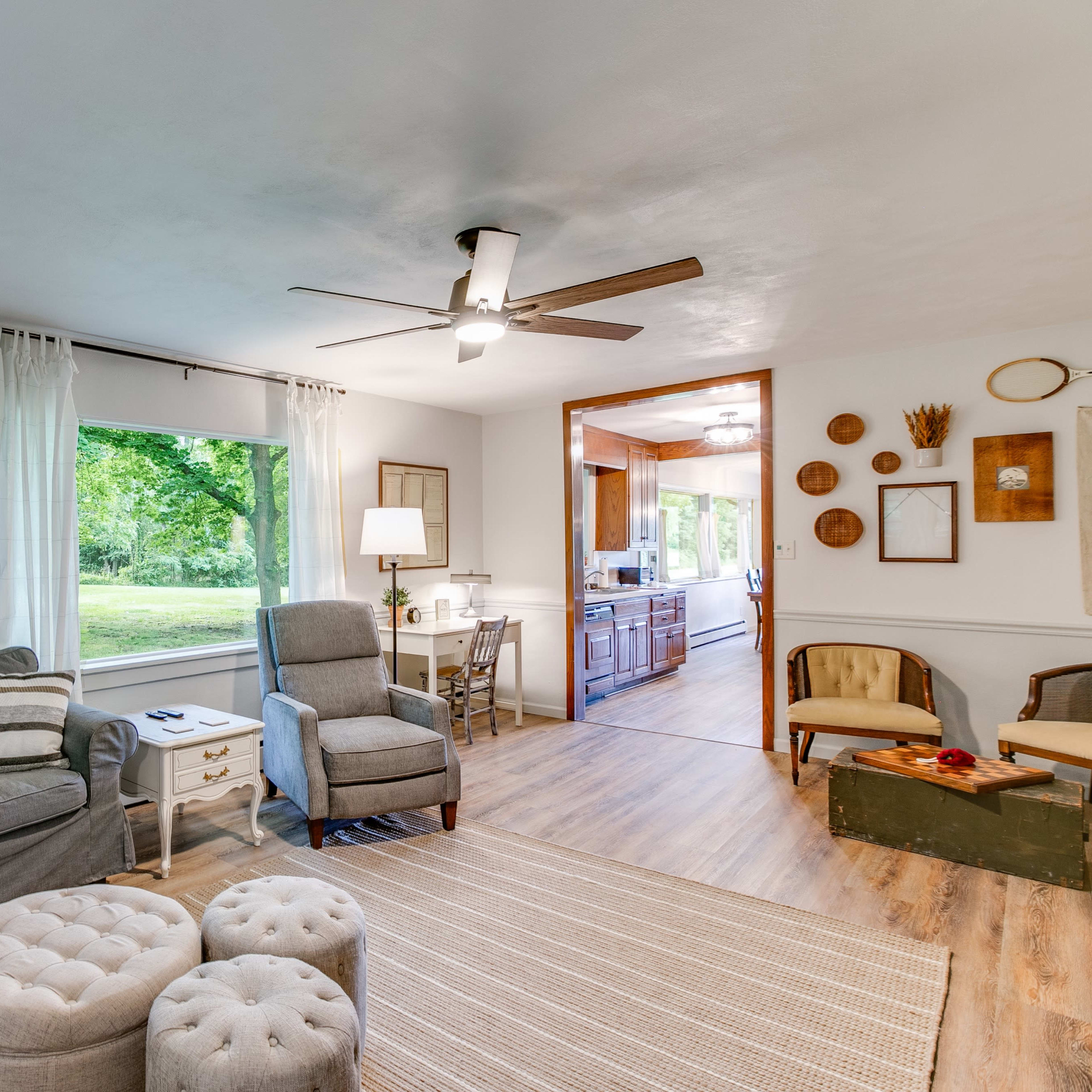 A cozy living room featuring a gray couch, a light fixture, and a view of a green outdoor area through a window.