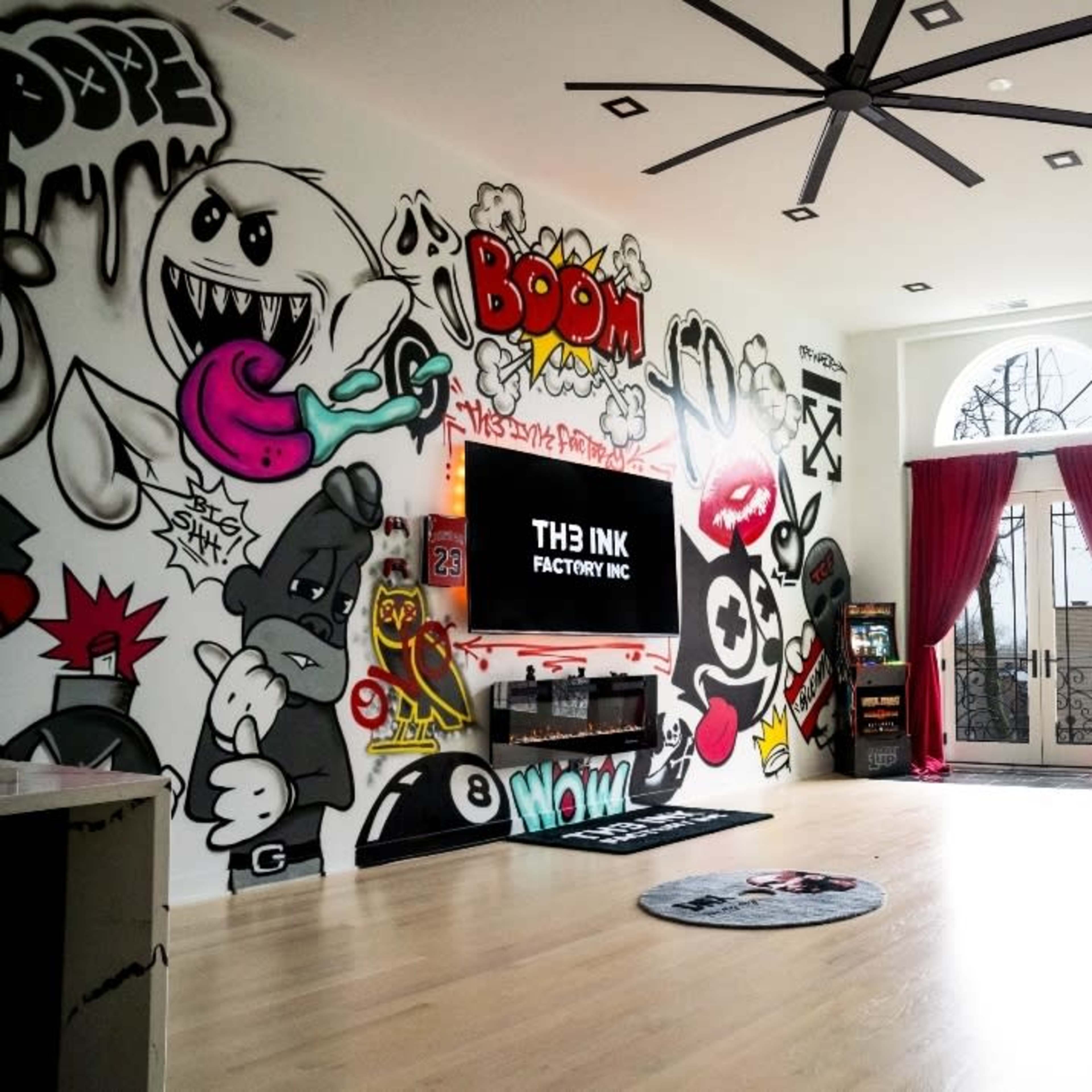 The room features a wall covered in colorful graffiti, a large television mounted on a sleek unit, and two red curtains framing a set of arched windows.