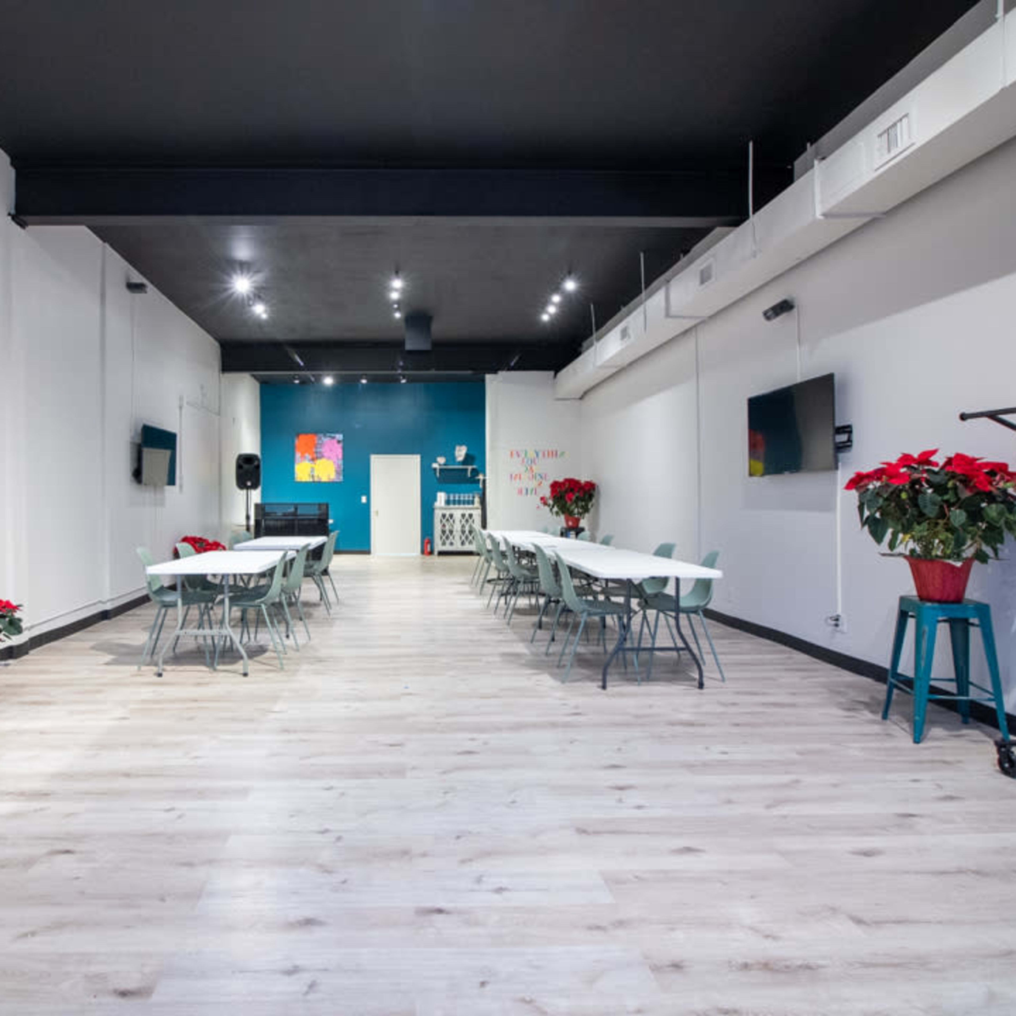 A spacious event room with multiple tables, chairs, a mirror on one wall, and red poinsettias arranged decoratively.
