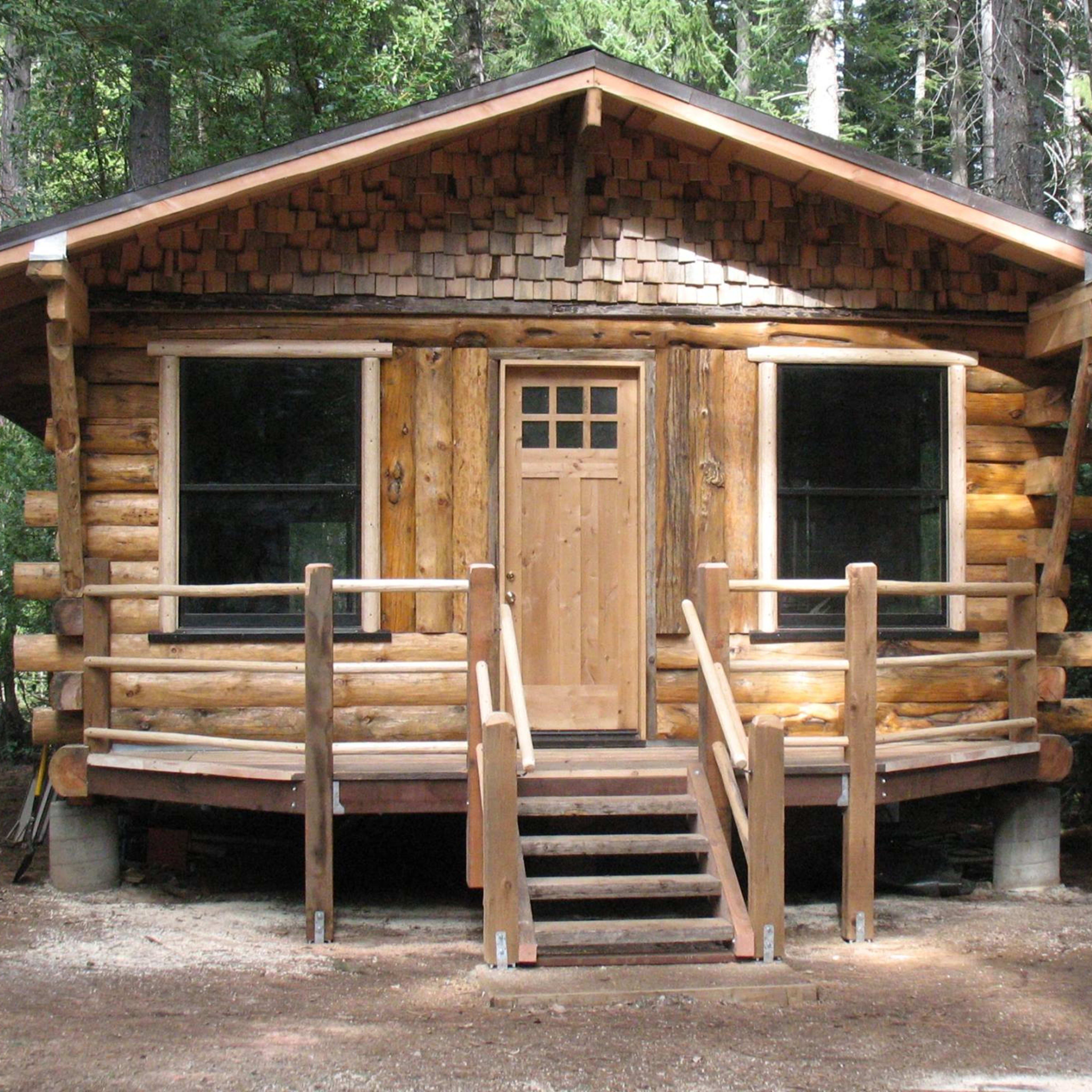 A wooden log cabin with a front porch and steps, surrounded by trees.