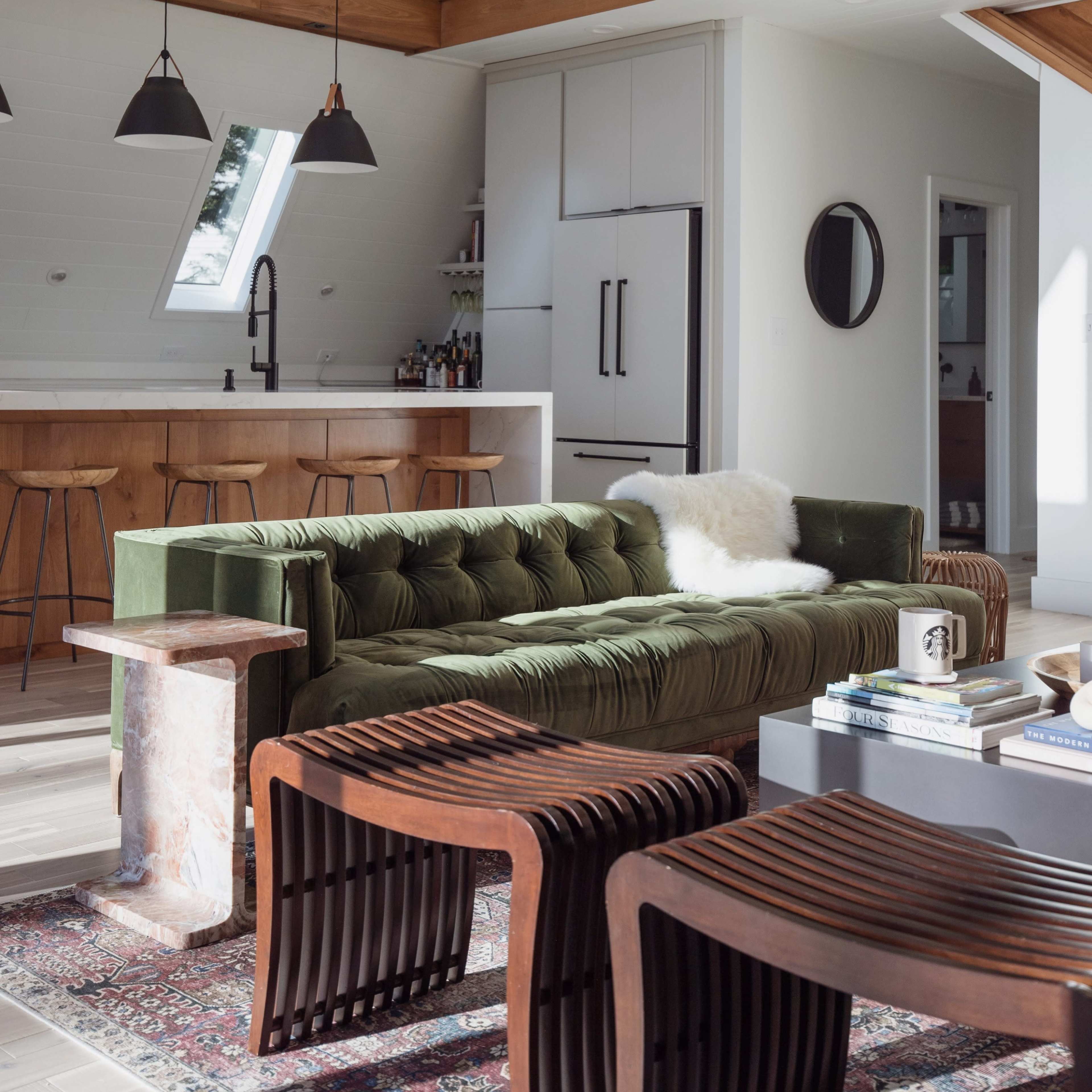 The scene features a modern living area with a green velvet sofa, wooden accent furniture, and a minimalist kitchen in the background.