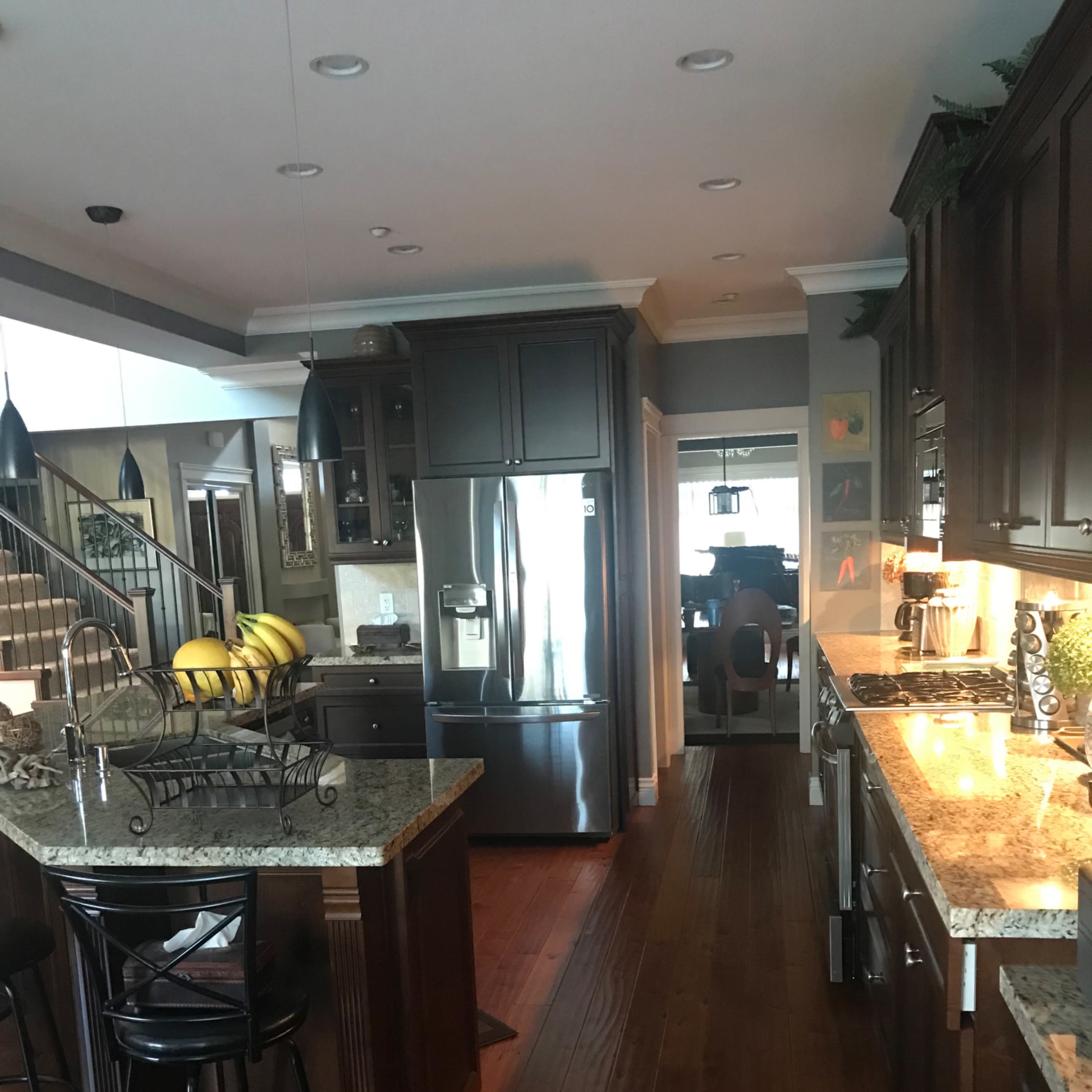 A modern kitchen with dark wooden cabinets, granite countertops, and a refrigerator next to a dining area.