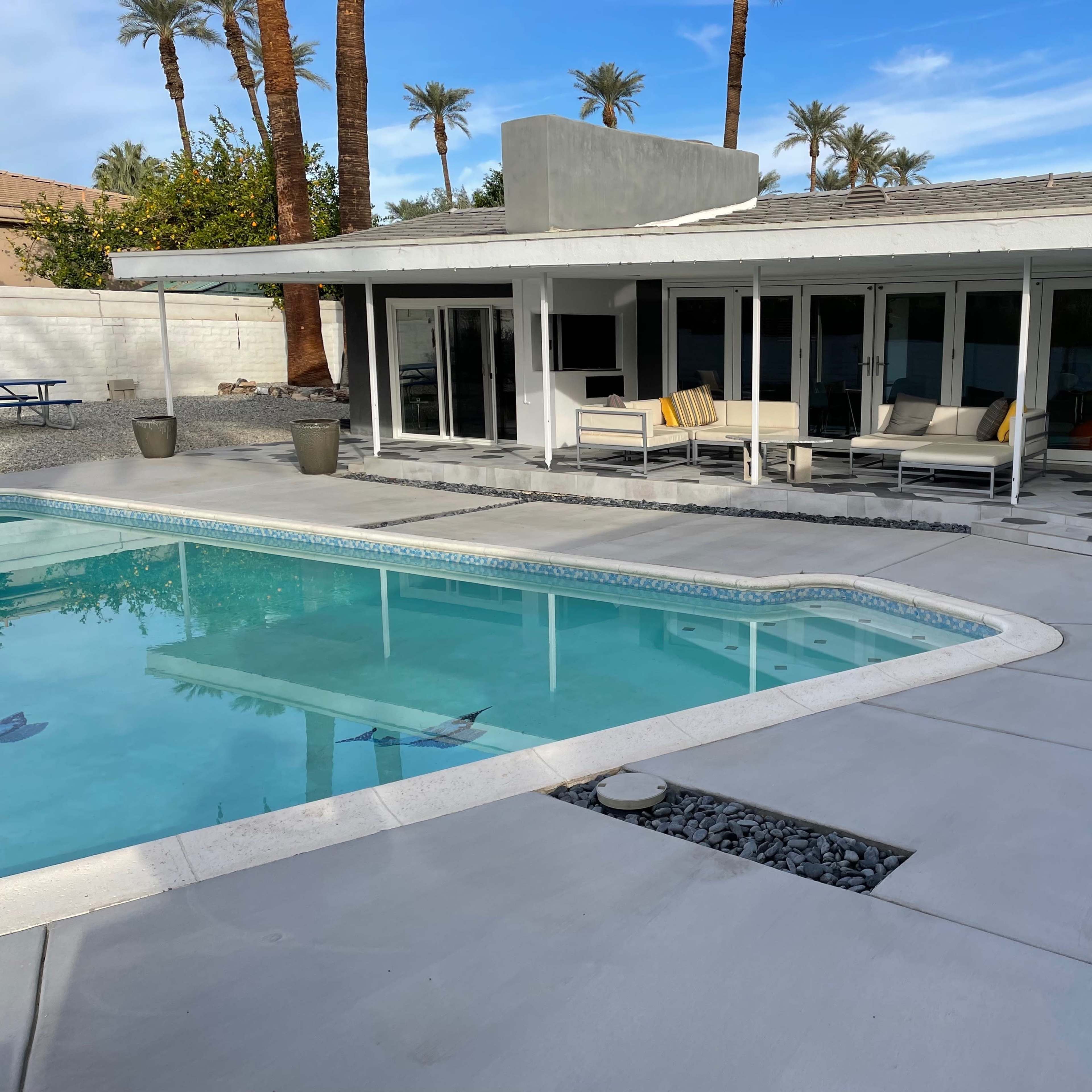 A modern backyard with a swimming pool, lounge chairs, and a covered patio area next to a house.