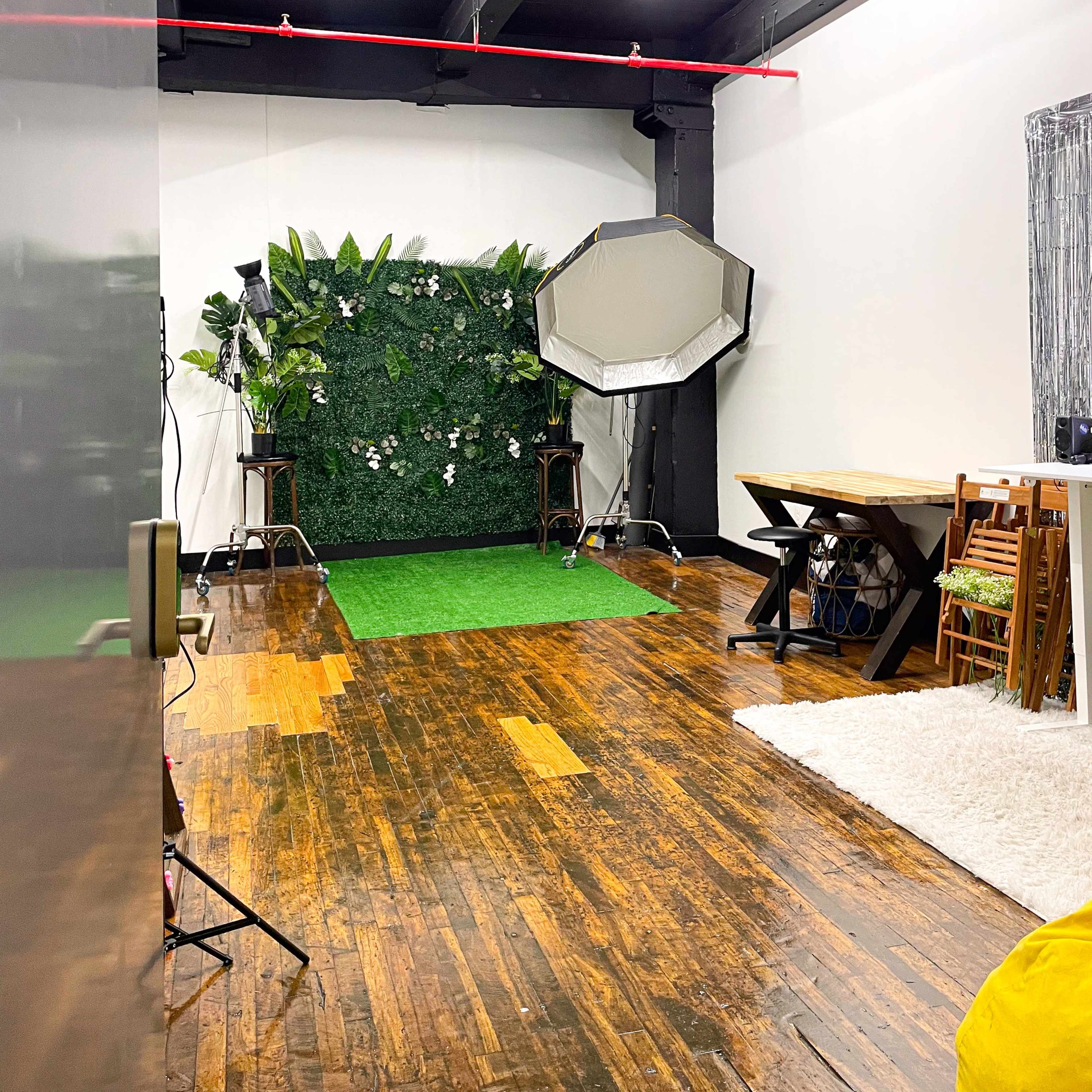 A photography studio with a green backdrop, wooden floors, and various lighting equipment.