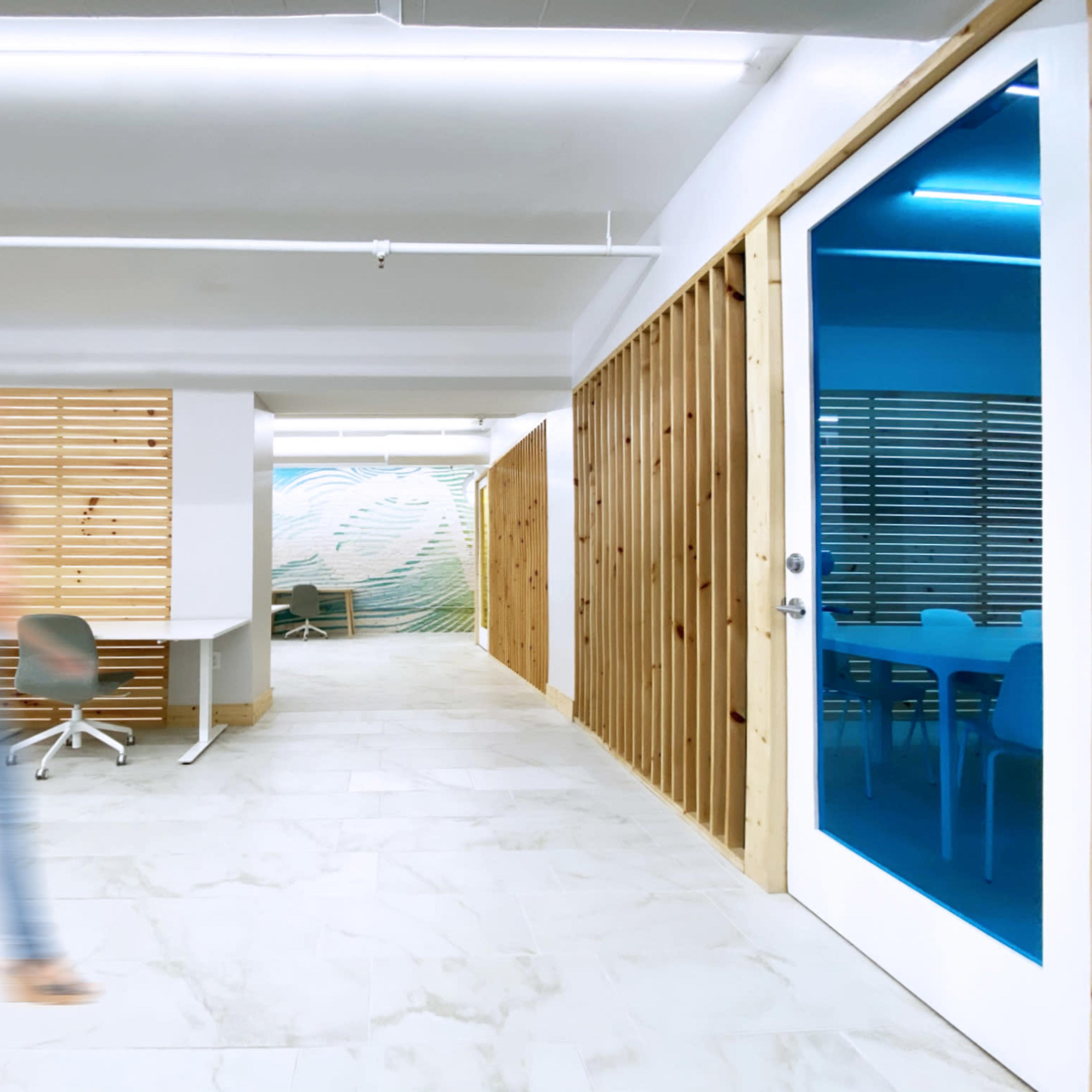 A person walks past a modern office space with wooden accents and a large mural on the wall.