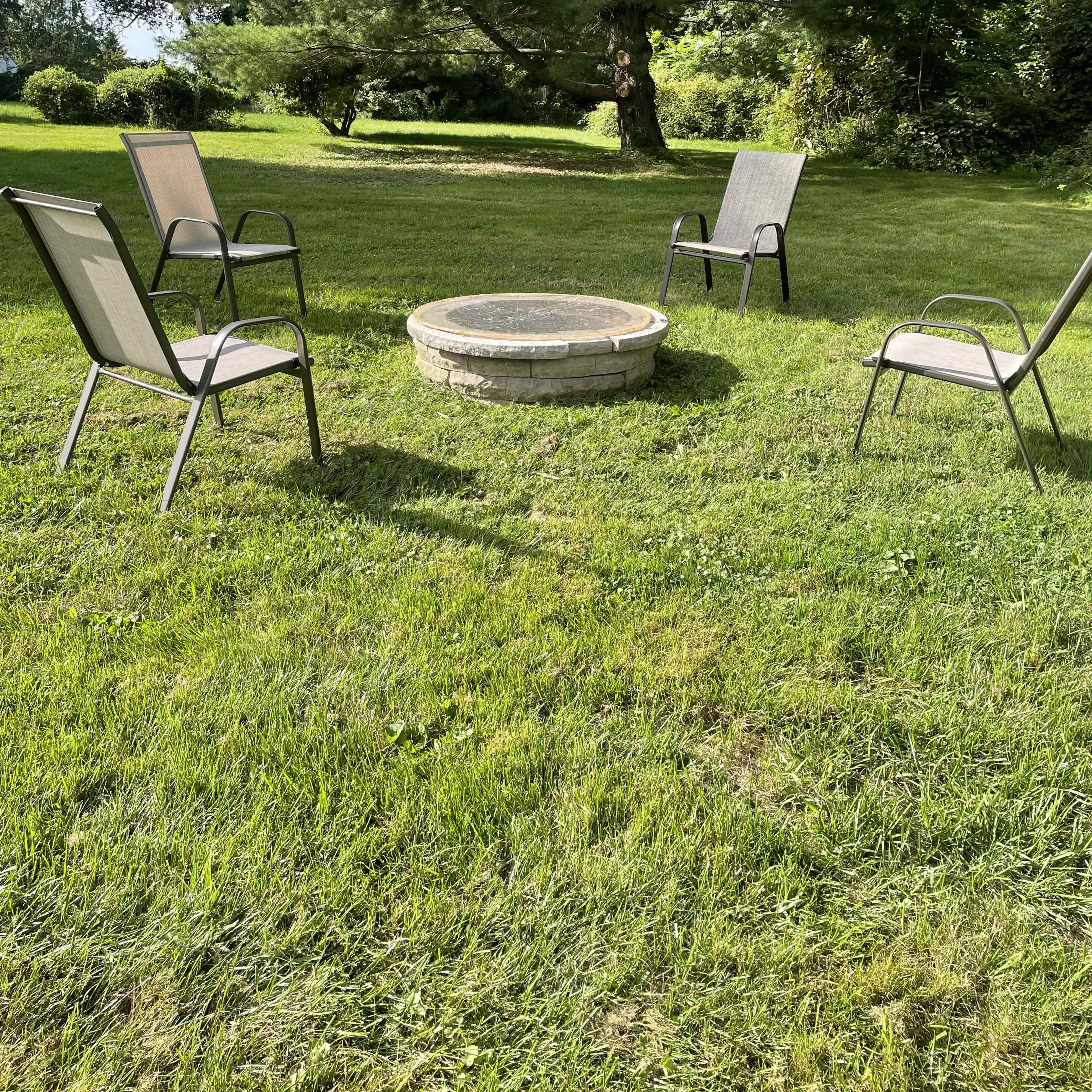 A stone fire pit surrounded by four metal chairs on a grassy lawn.