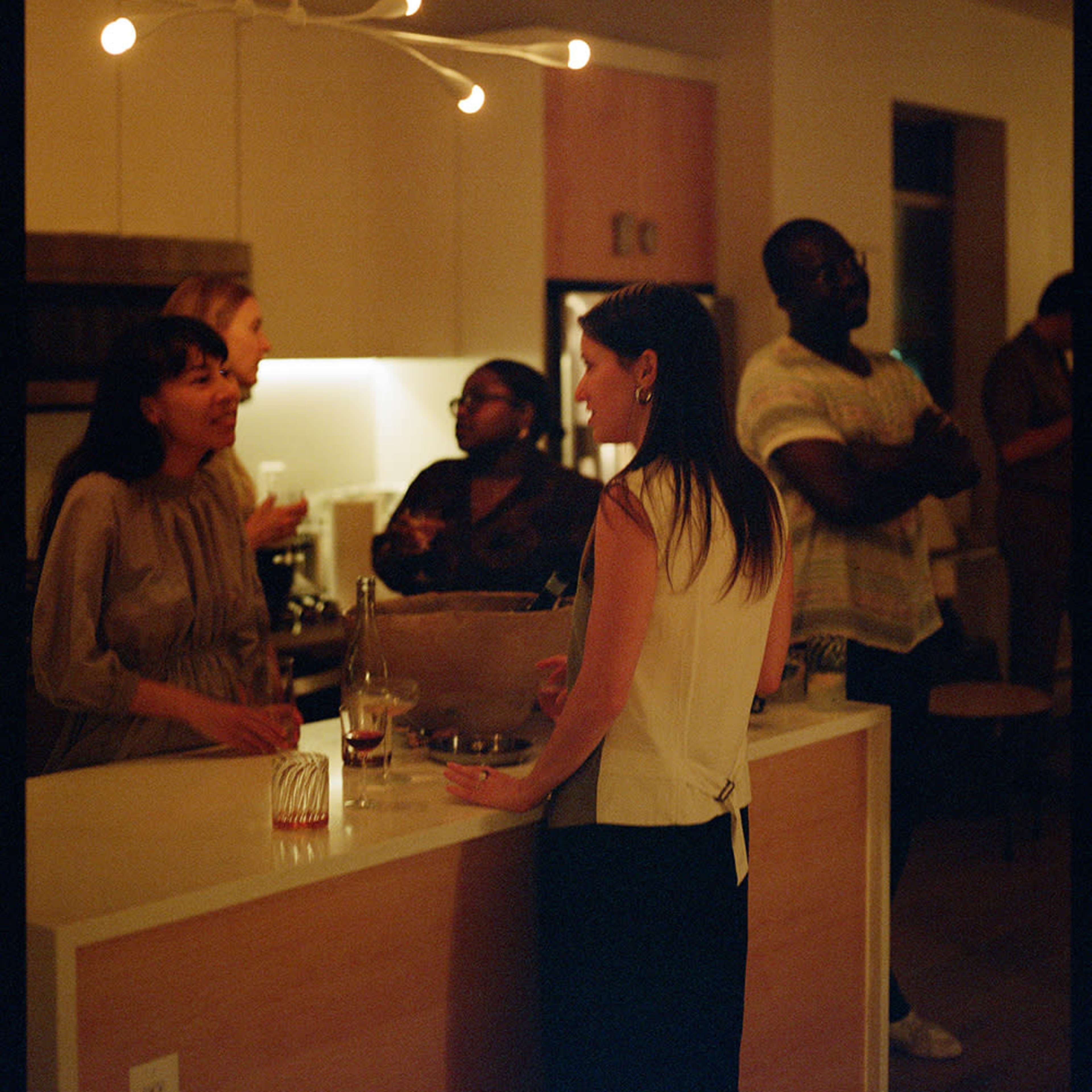 A group of people converse in a cozy kitchen setting with warm lighting and modern decor.