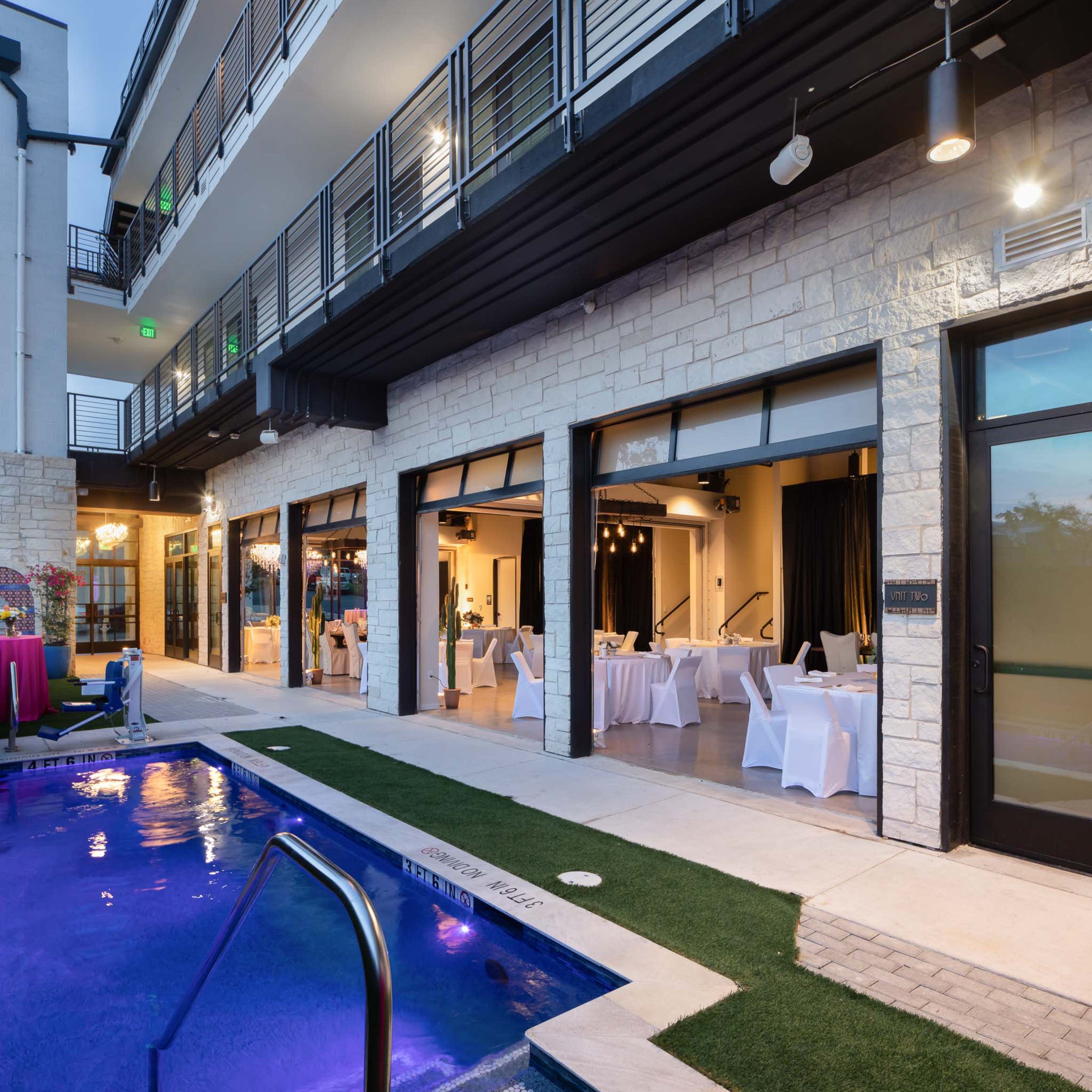 A modern building with a lounge area overlooking a pool, featuring large glass doors that open to a banquet room with tables set for dining.
