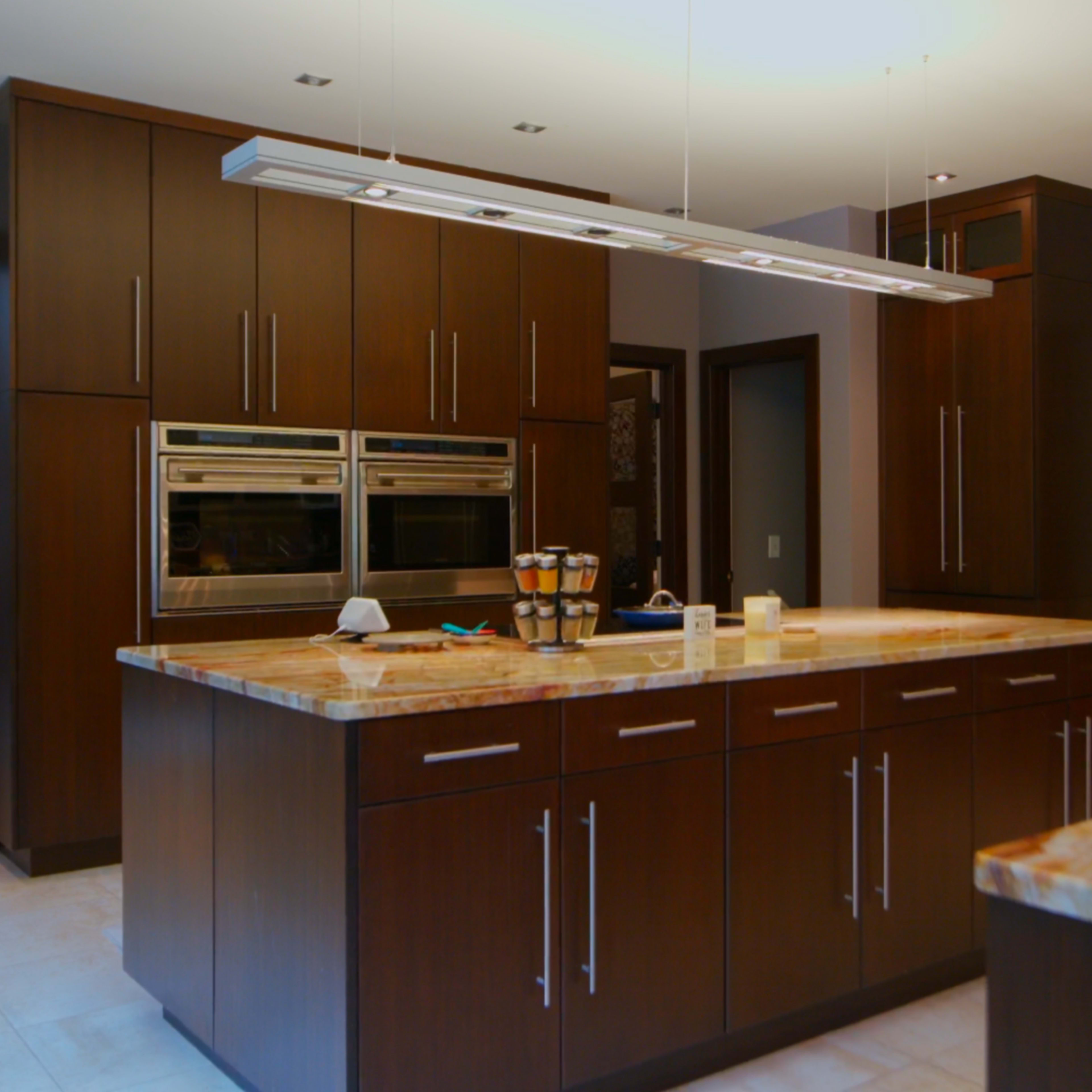 A modern kitchen with dark wood cabinets, double wall ovens, and a large island featuring a patterned countertop.