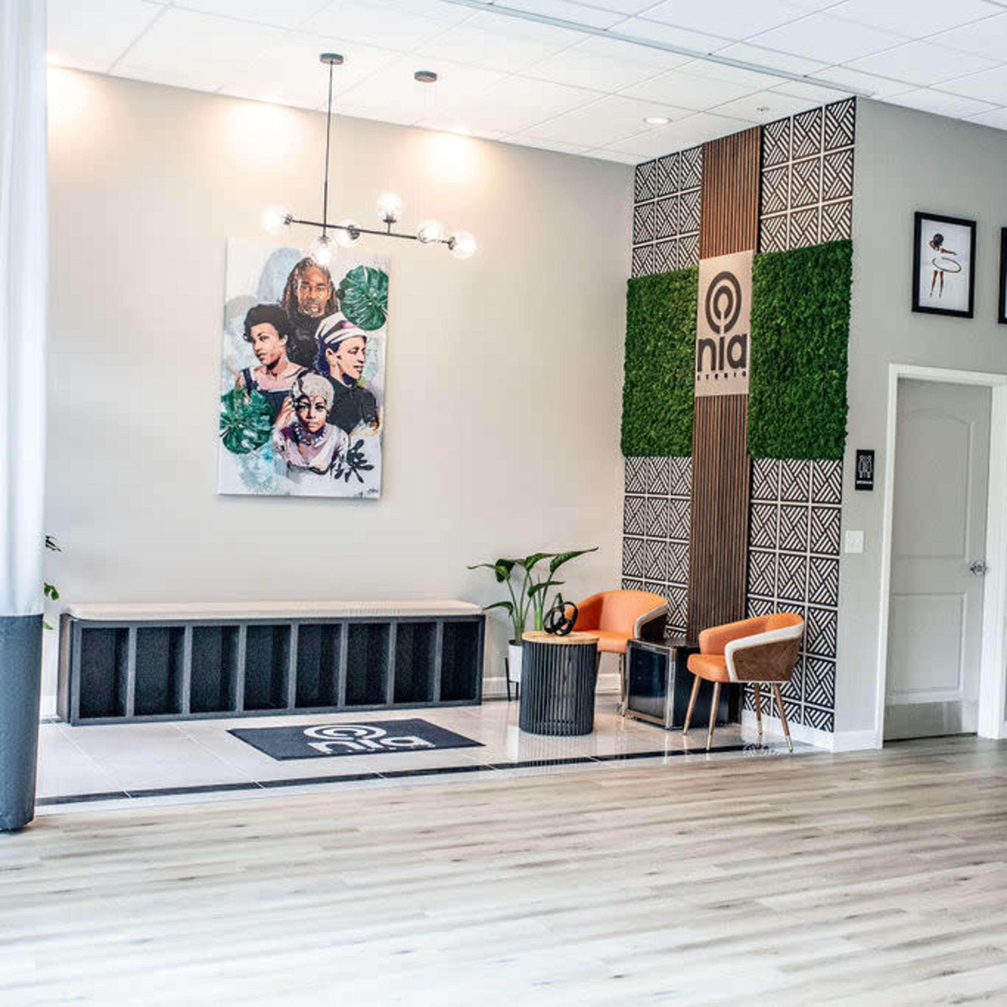 A modern interior space featuring a seating area with two orange chairs, decorative wall art, and a green plant against a stylish backdrop.
